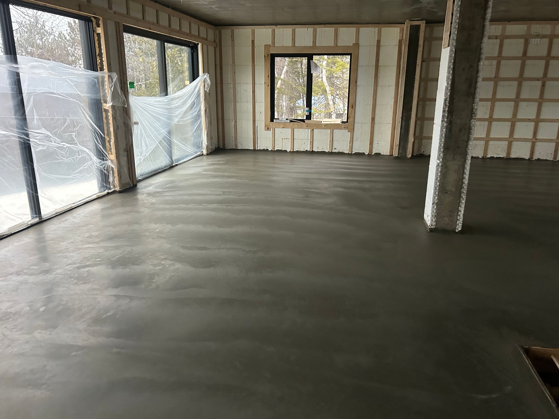 Sol en béton fraîchement coulé à l'intérieur d'une pièce avec de grandes fenêtres et des murs non finis.