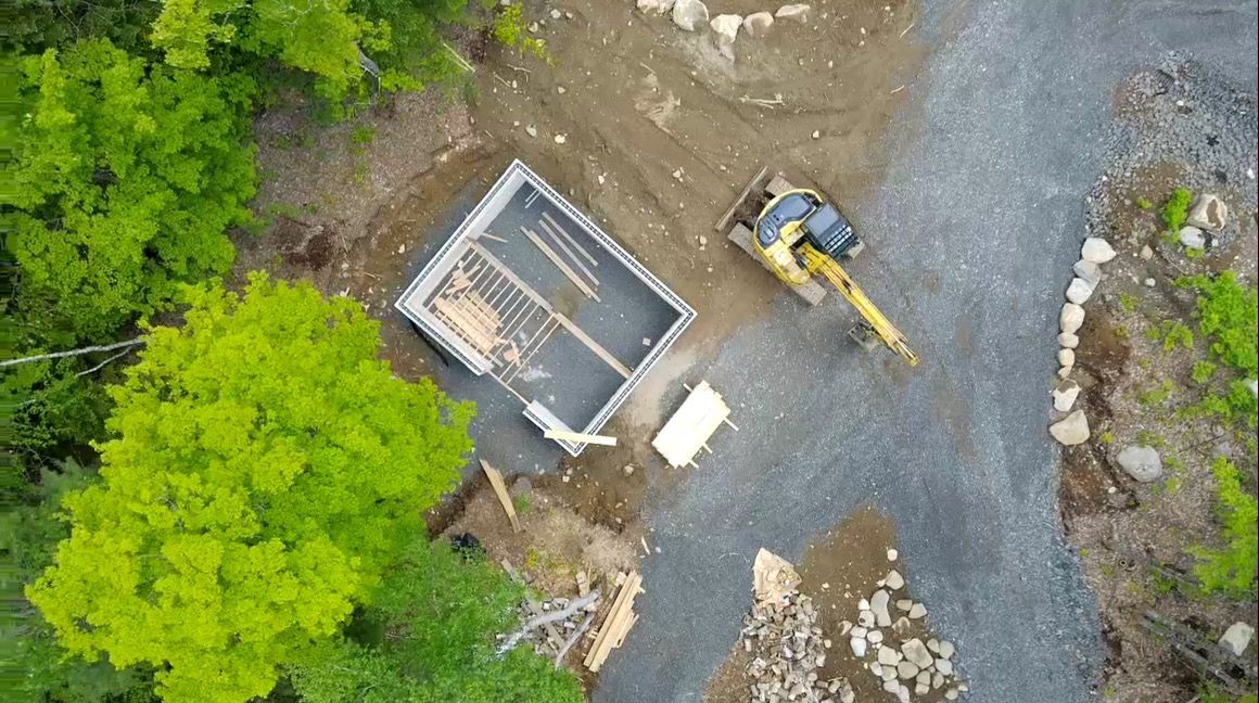 Vue aérienne d'un chantier de construction avec une excavatrice et des fondations dans une zone de gravier.