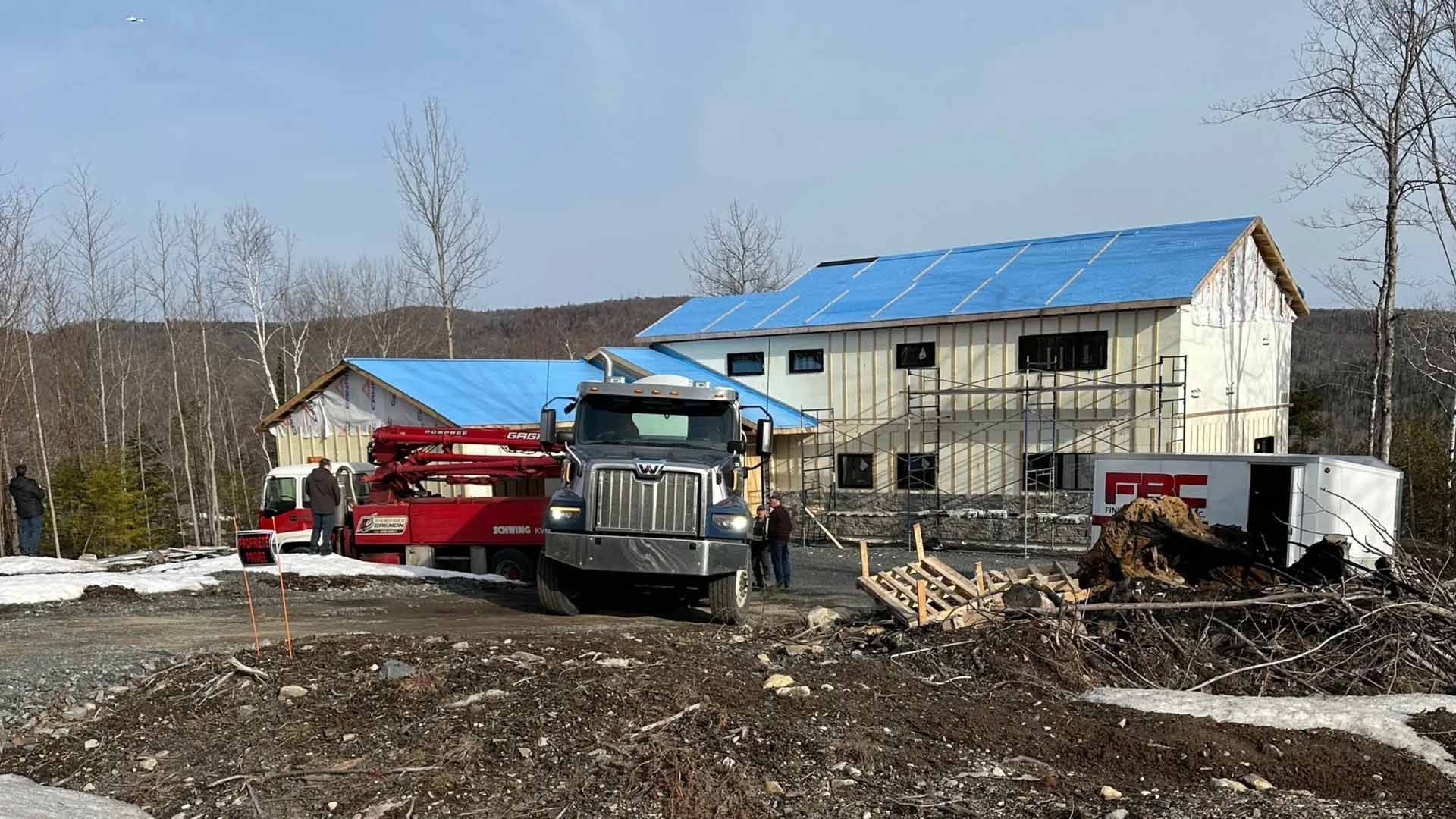 Chantier : un camion et du matériel sont stationnés devant une maison en construction, dont le toit est recouvert de bâches bleues.