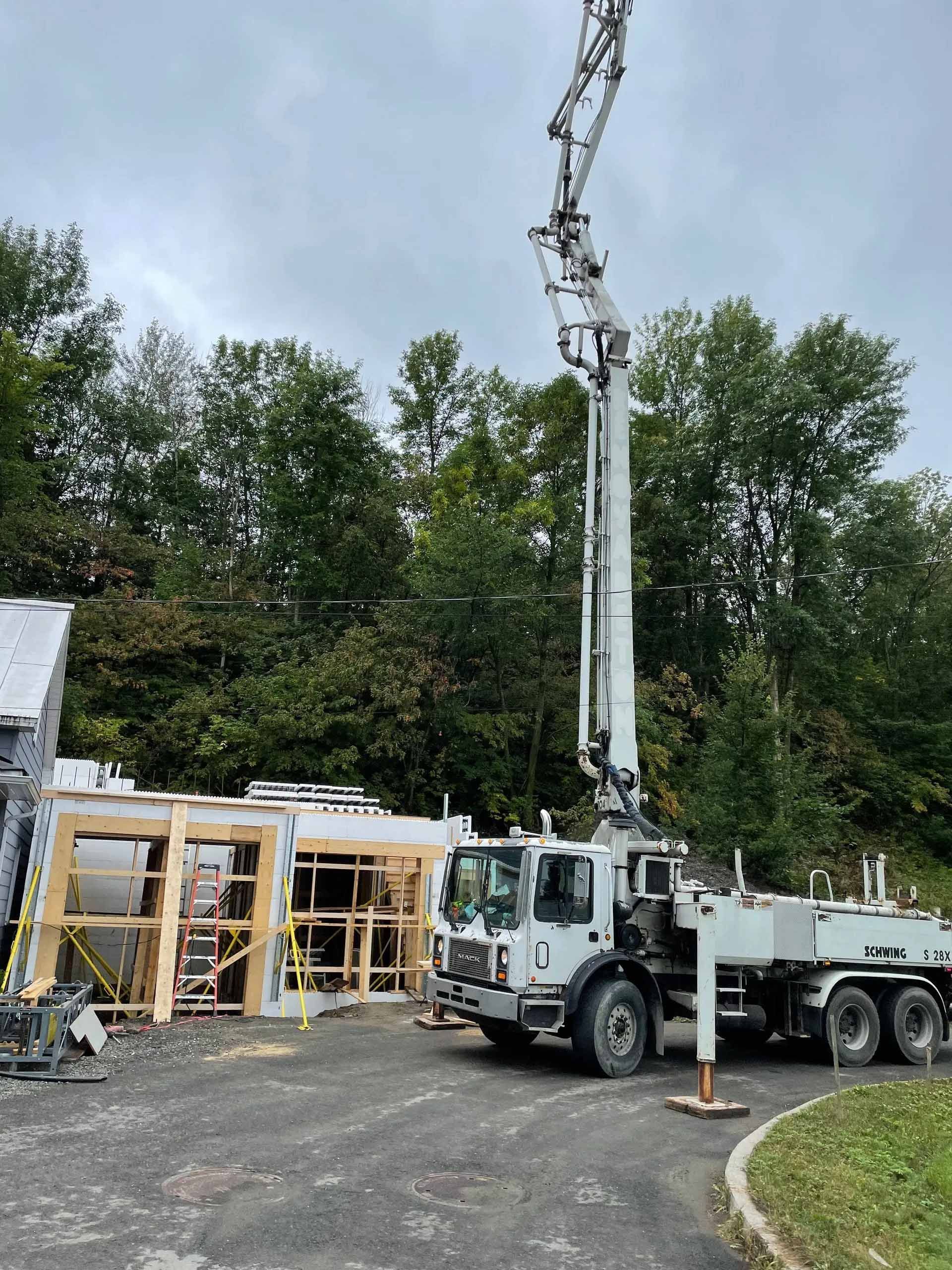 Camion-pompe à béton déversant du béton dans une structure à ossature bois près des arbres. Ciel nuageux.