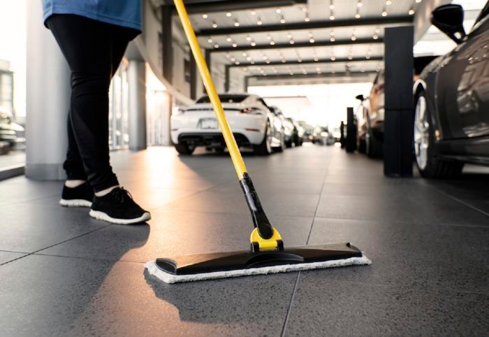 Person mopping the floor of a car dealership, cars in the background.
