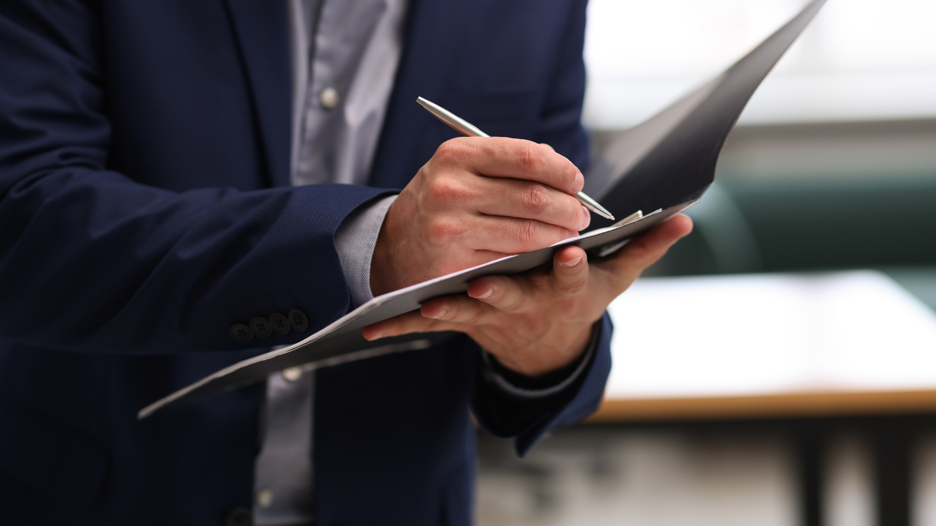 Person in a dark suit writing on a clipboard with a pen