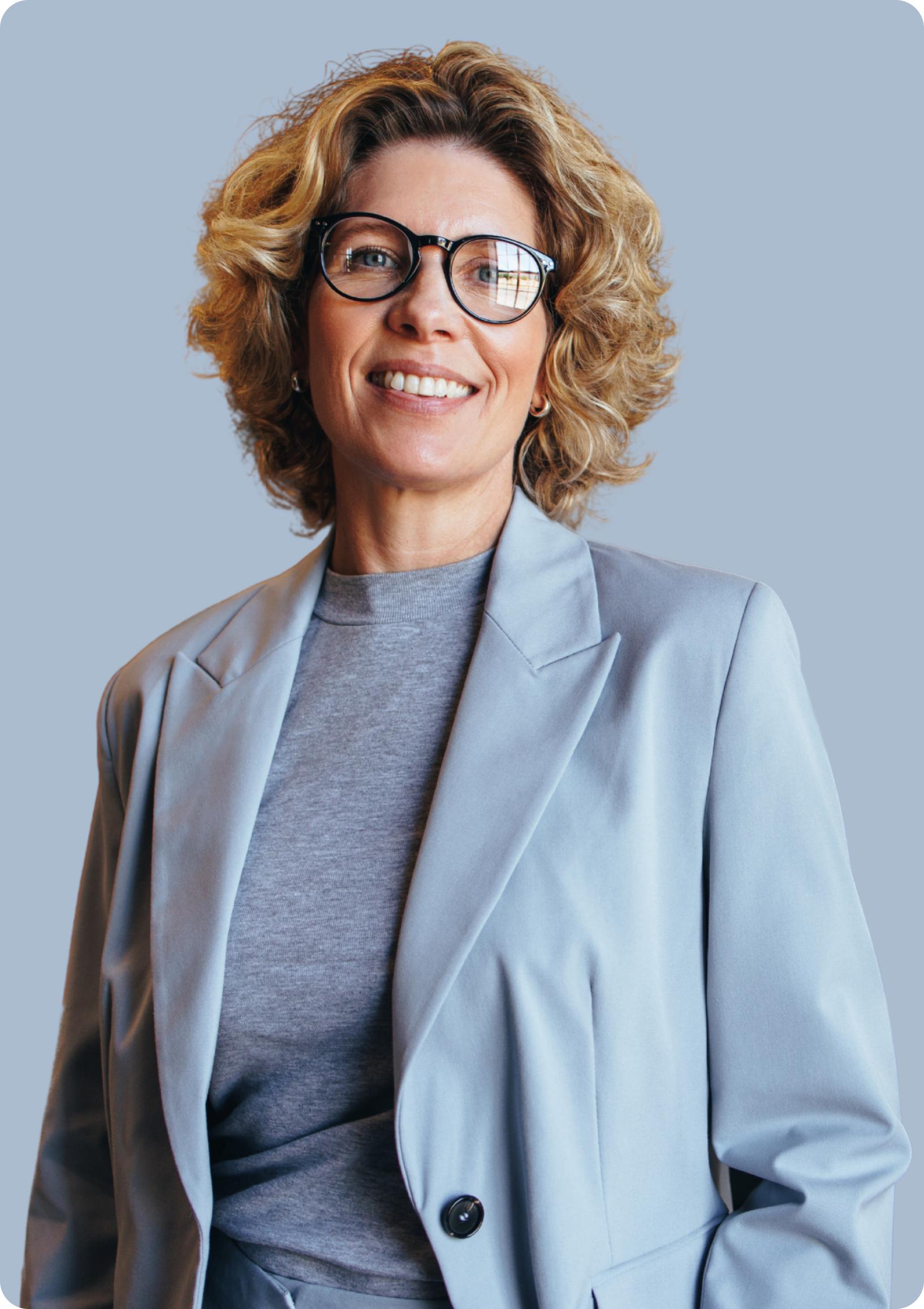 A woman wearing glasses and a blue jacket is smiling.