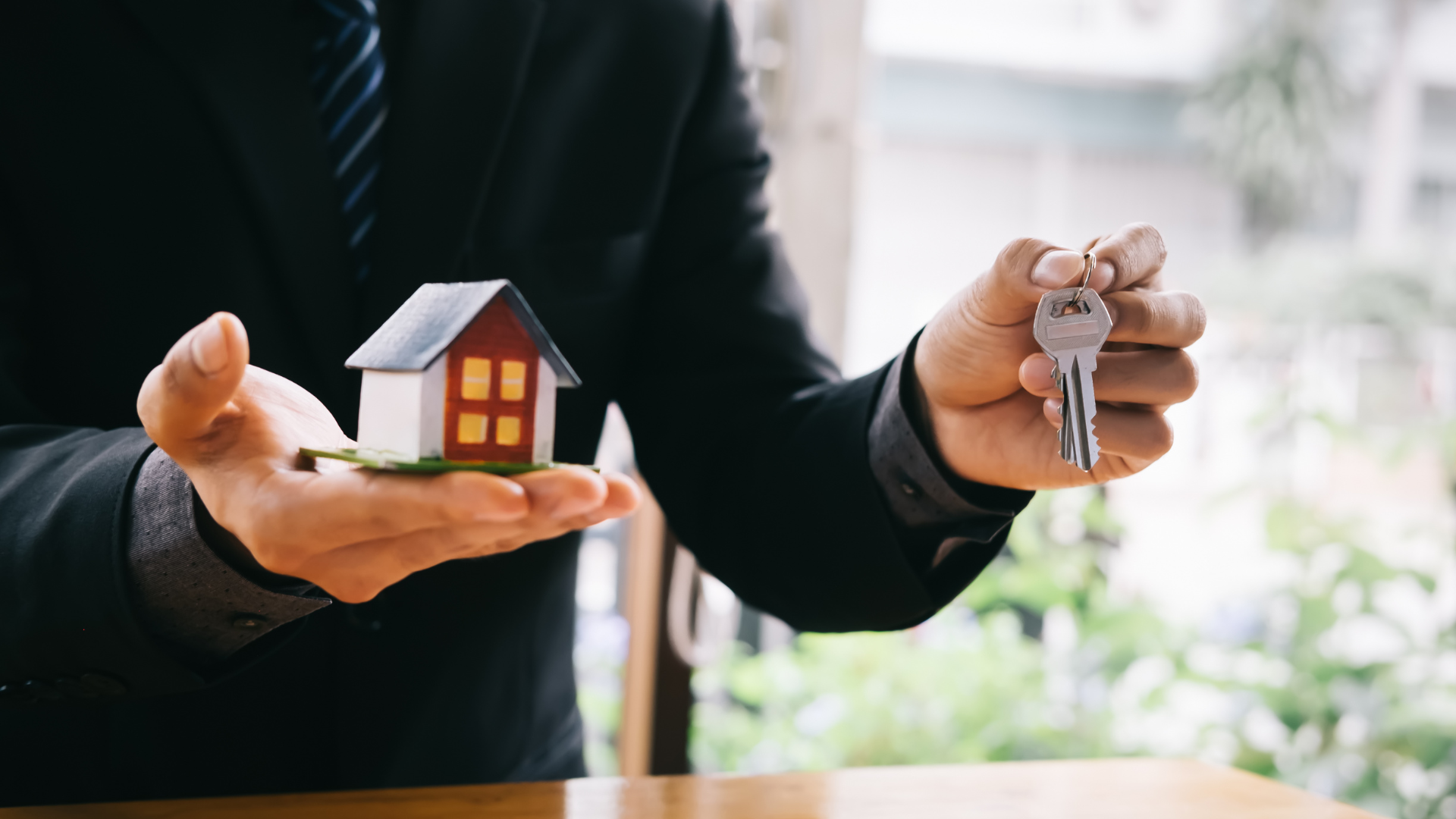 A man in a suit is holding a model house and keys.