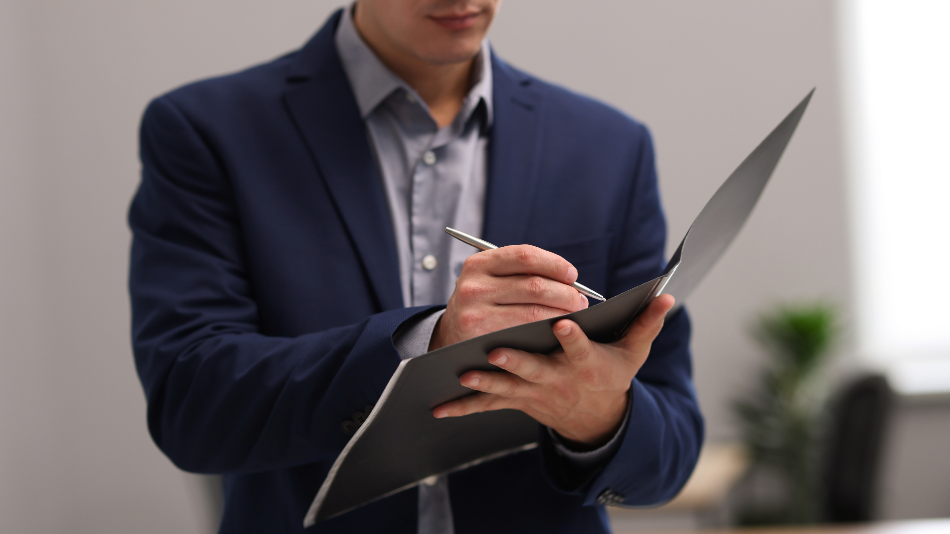 Business professional holding a black folder and writing with a stylus in an office setting