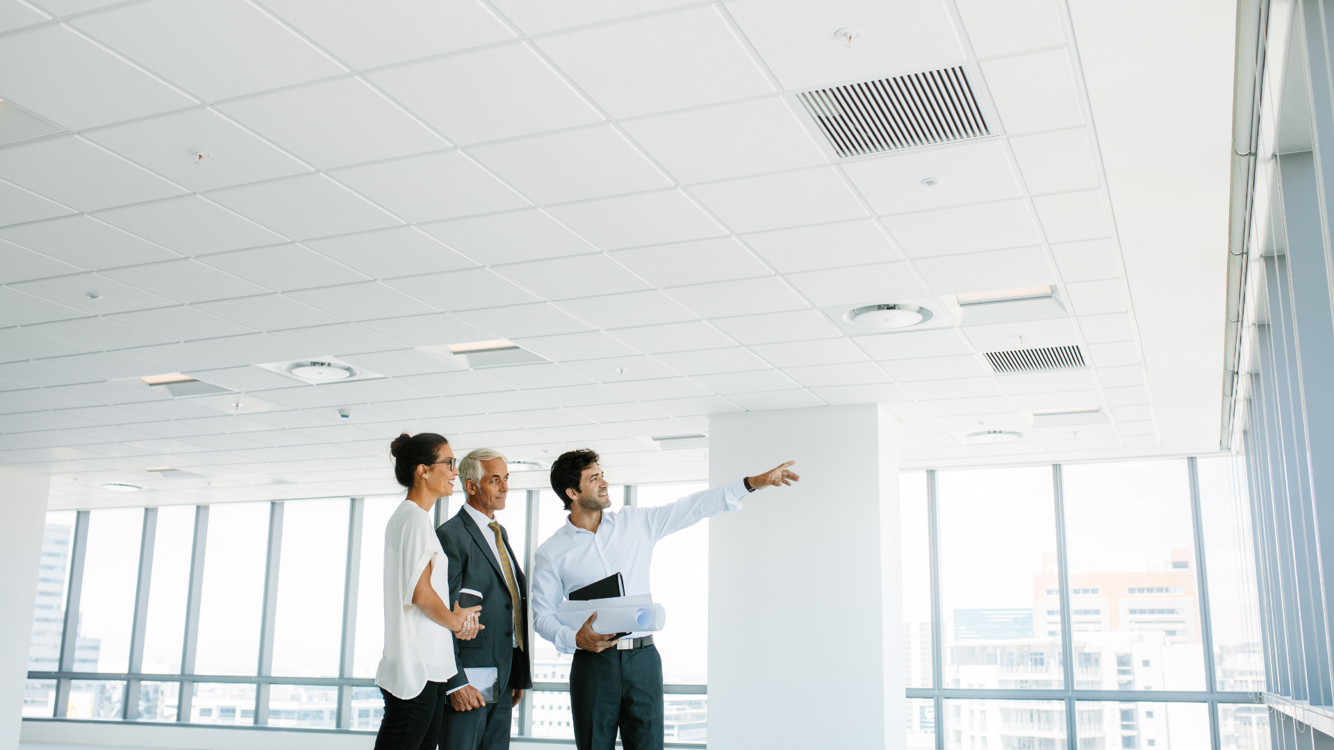 A group of people are standing in an empty office building looking up at the ceiling.