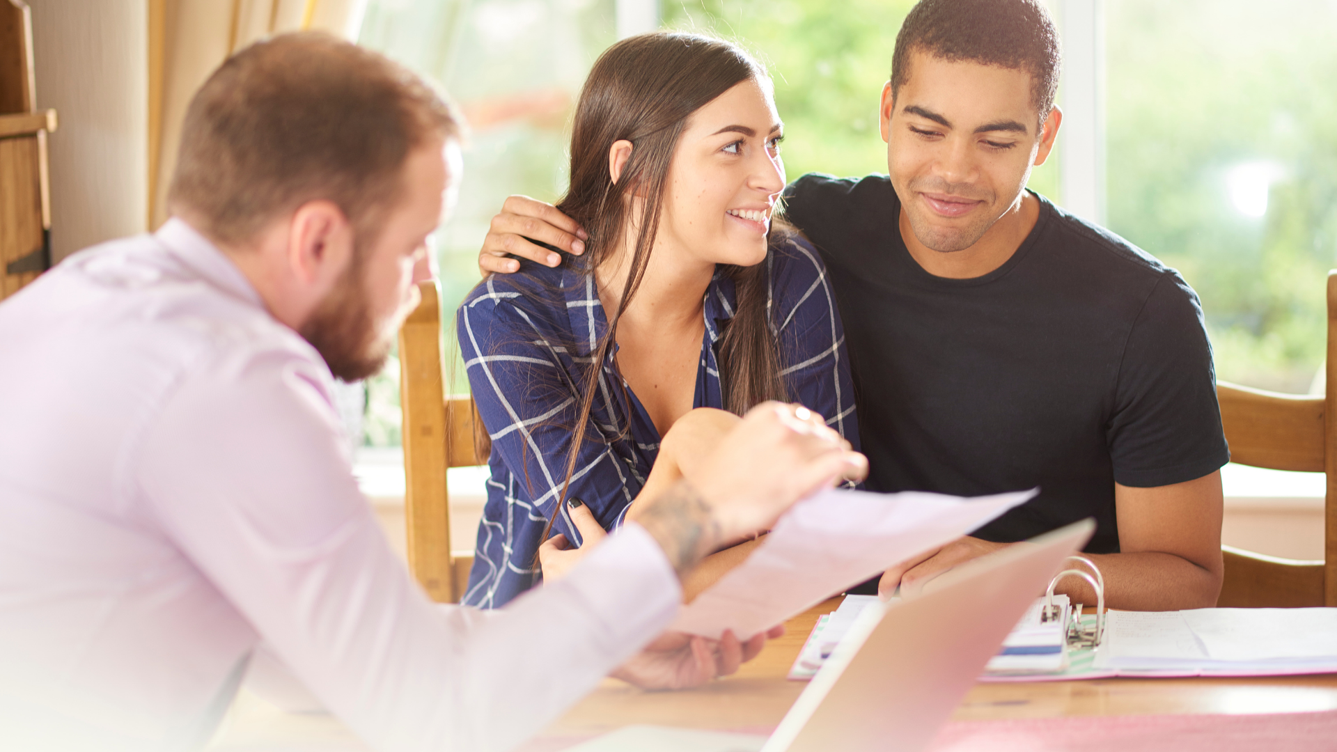 A couple sits with a financial advisor, reviewing documents at a table.