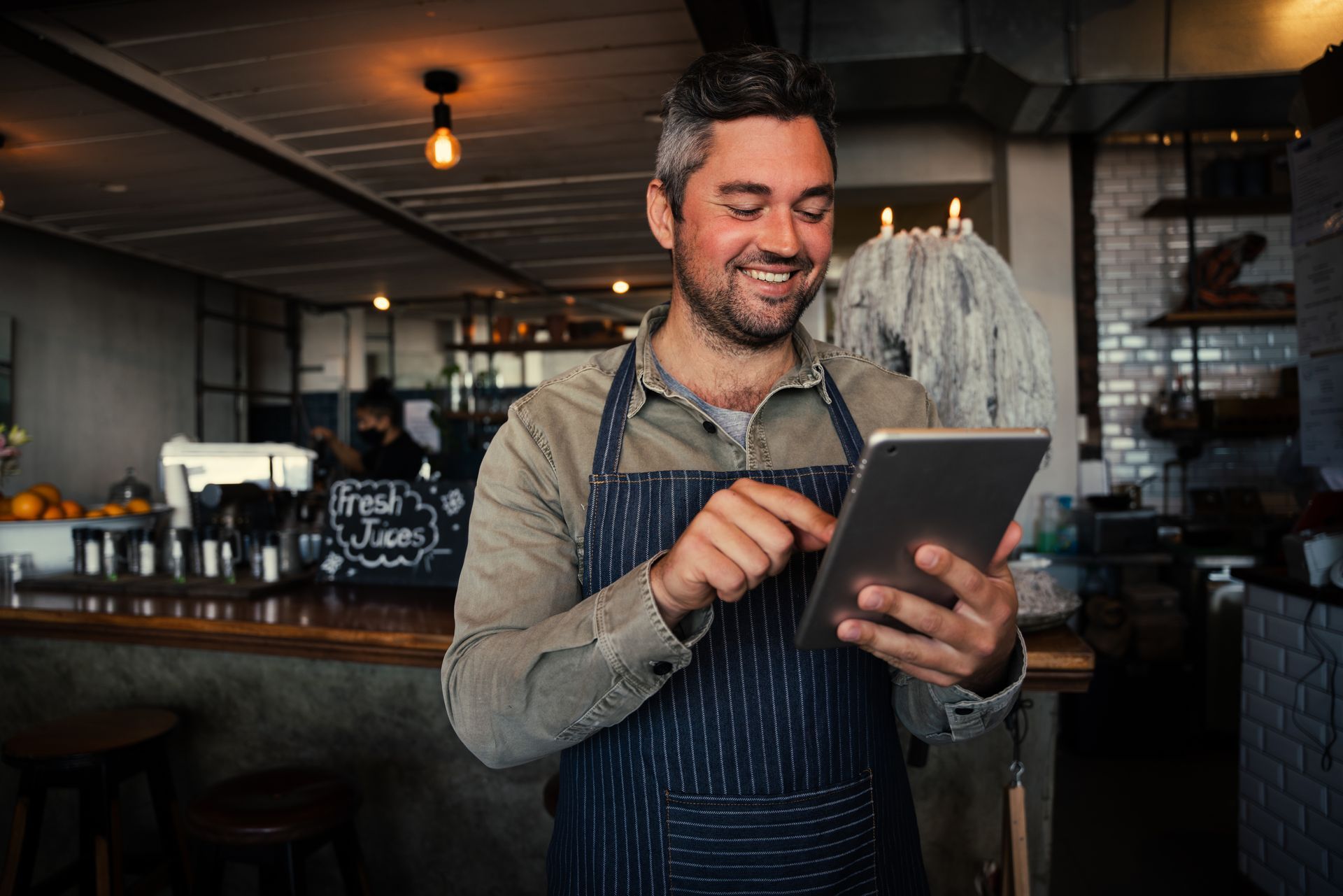A man in an apron is using a tablet in a restaurant.