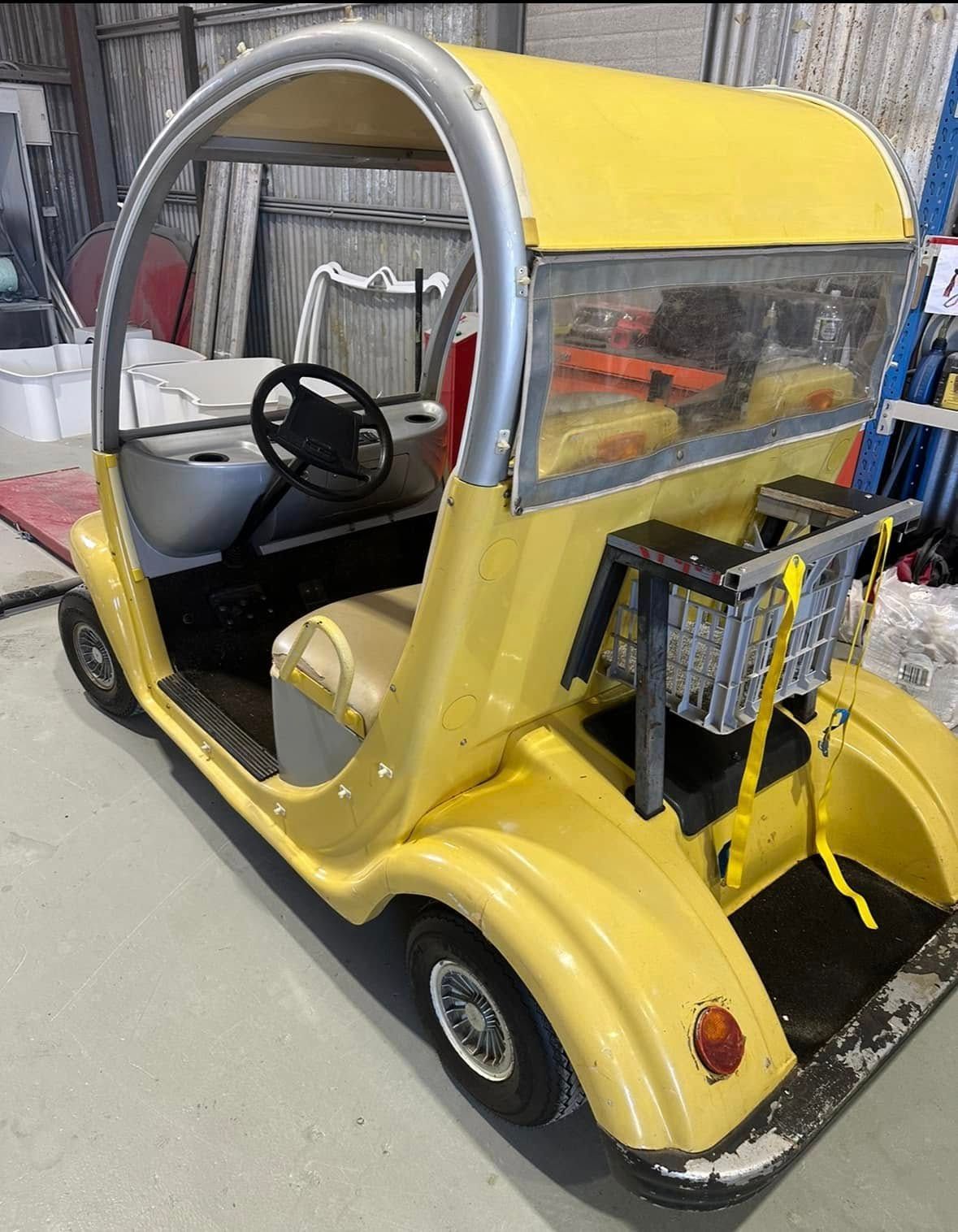 A yellow golf cart with a basket on the back is parked in a garage.