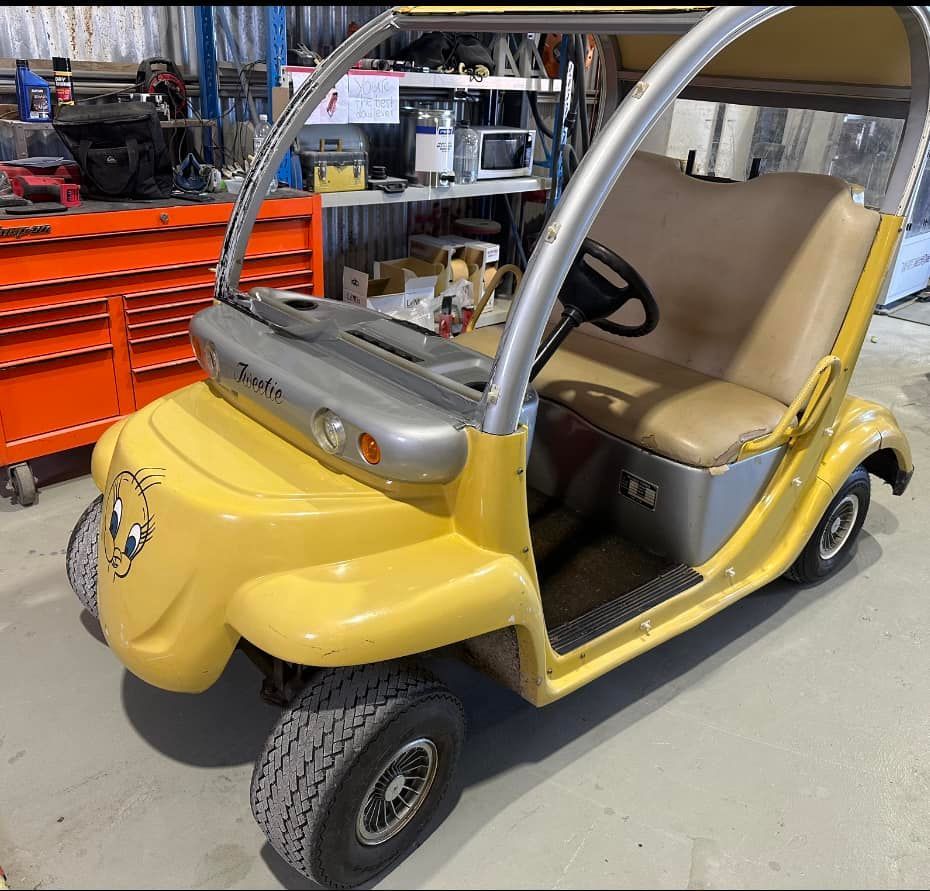A yellow golf cart with a smiley face on the front is parked in a garage