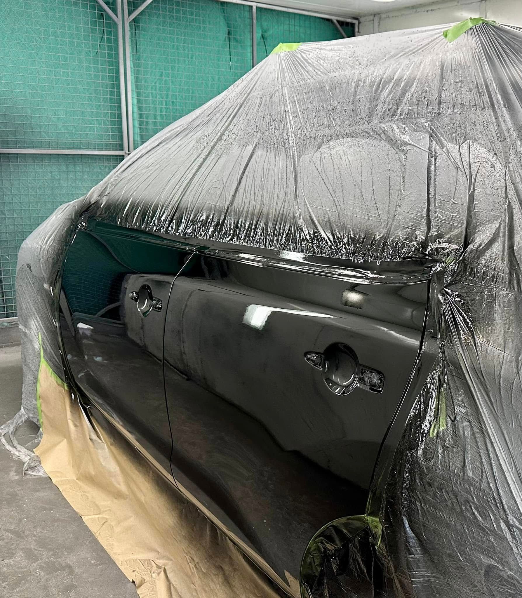 A car is covered in a black tarp in a garage.