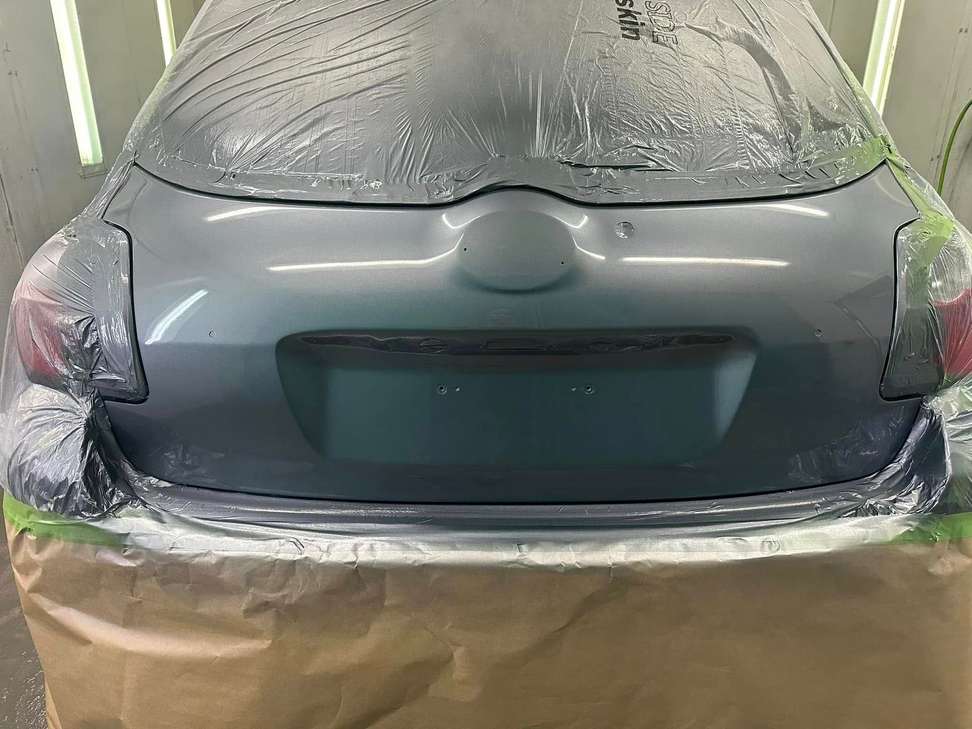 The back of a car is covered in plastic and is being painted.