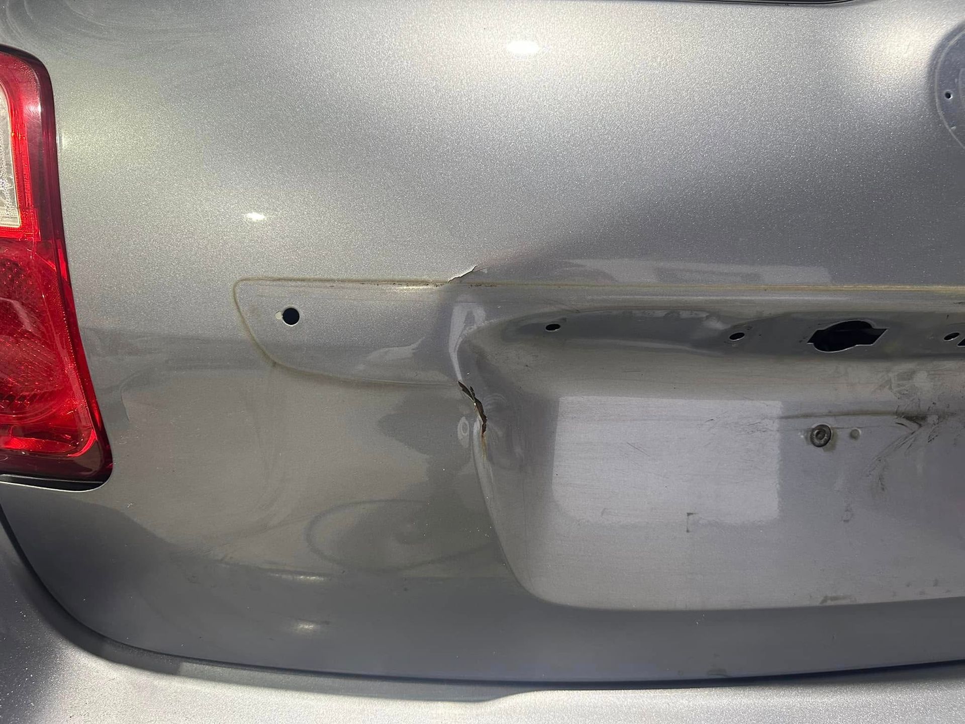 A close up of the back of a silver car with a damaged bumper.