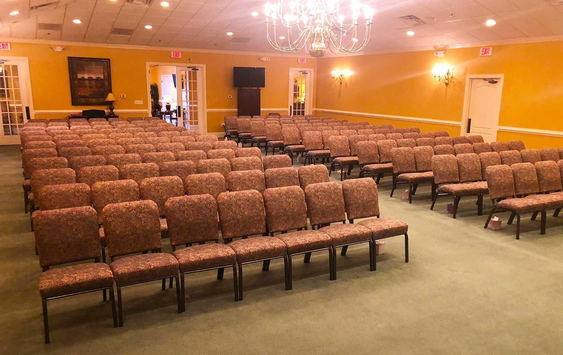 Rows of brown patterned chairs in a yellow-walled room with a chandelier and multiple doors.
