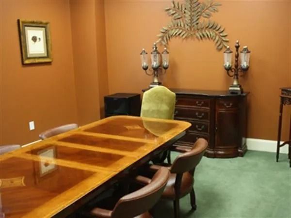 An office dining room with brown walls, wooden table, chairs, and ornate buffet.