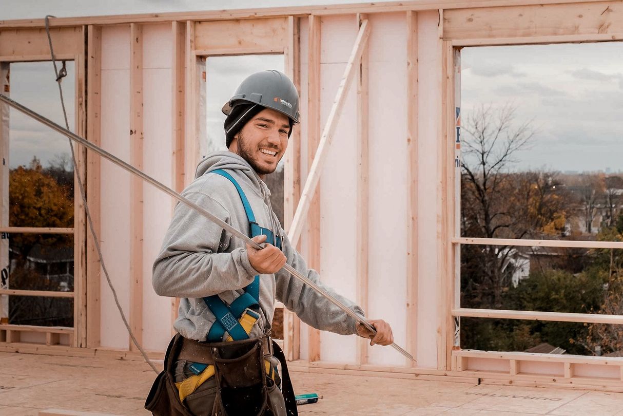Ouvrier du bâtiment tenant une barre d'armature, souriant. Intérieur avec fenêtres en arrière-plan.