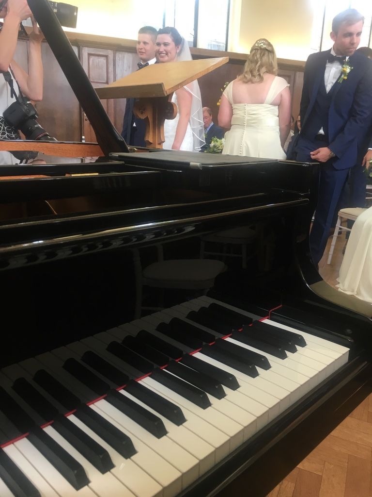 A grand piano with an open lid in front of a smiling bride and groom