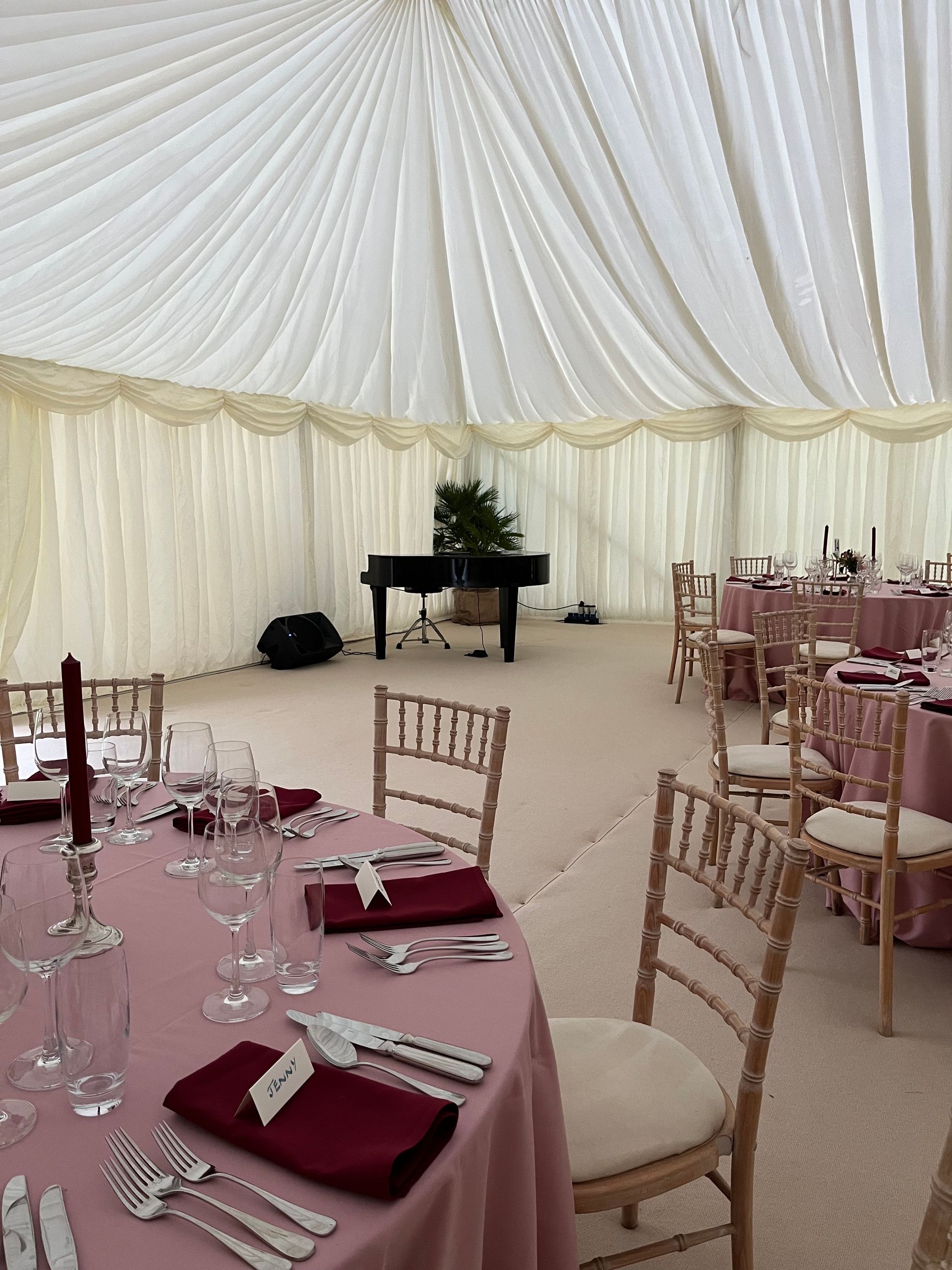 Black grand piano in the corner of a marquee set up for a wedding