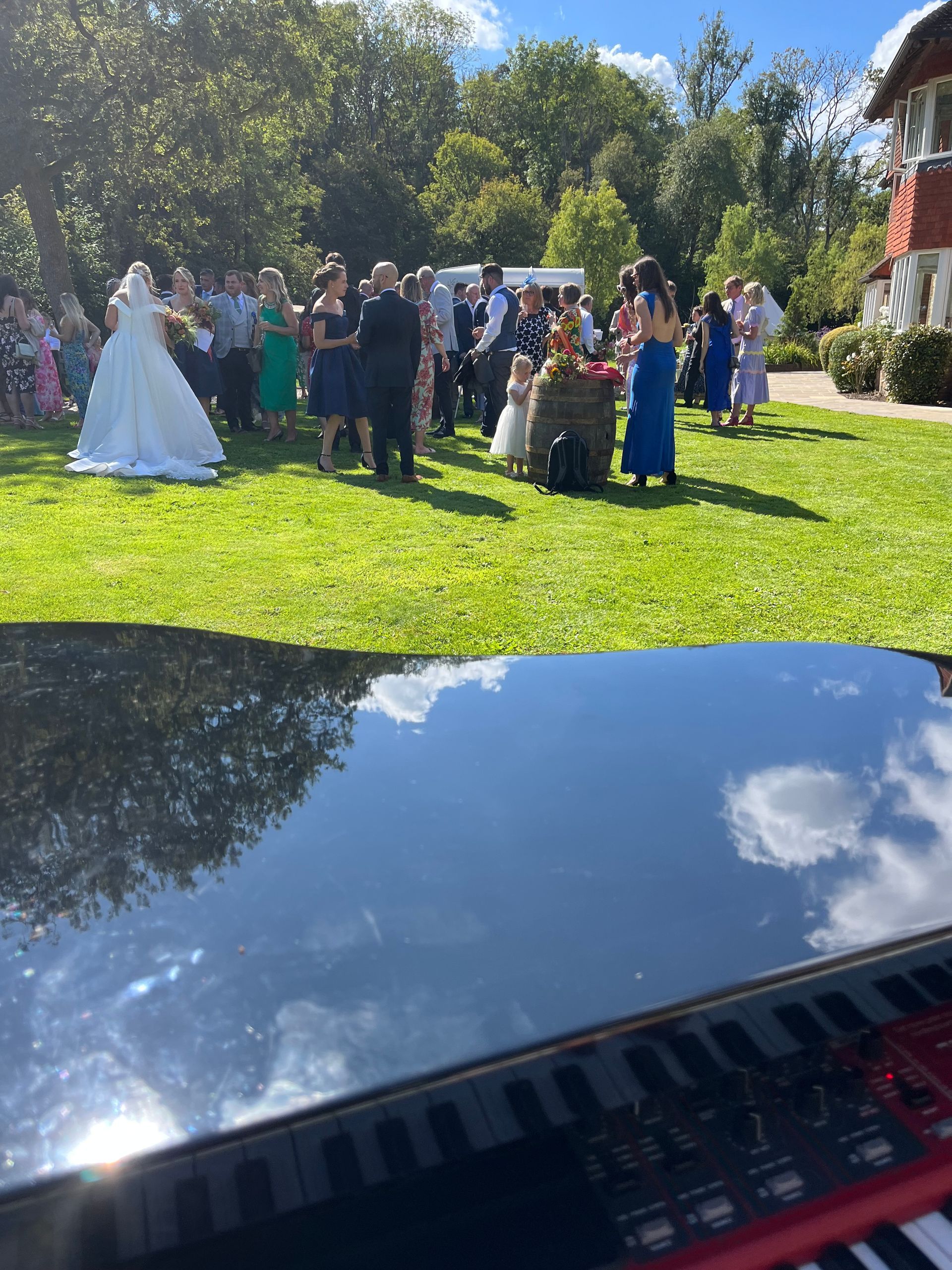 A black grand piano in a garden overlooking a bride & groom and all their guests