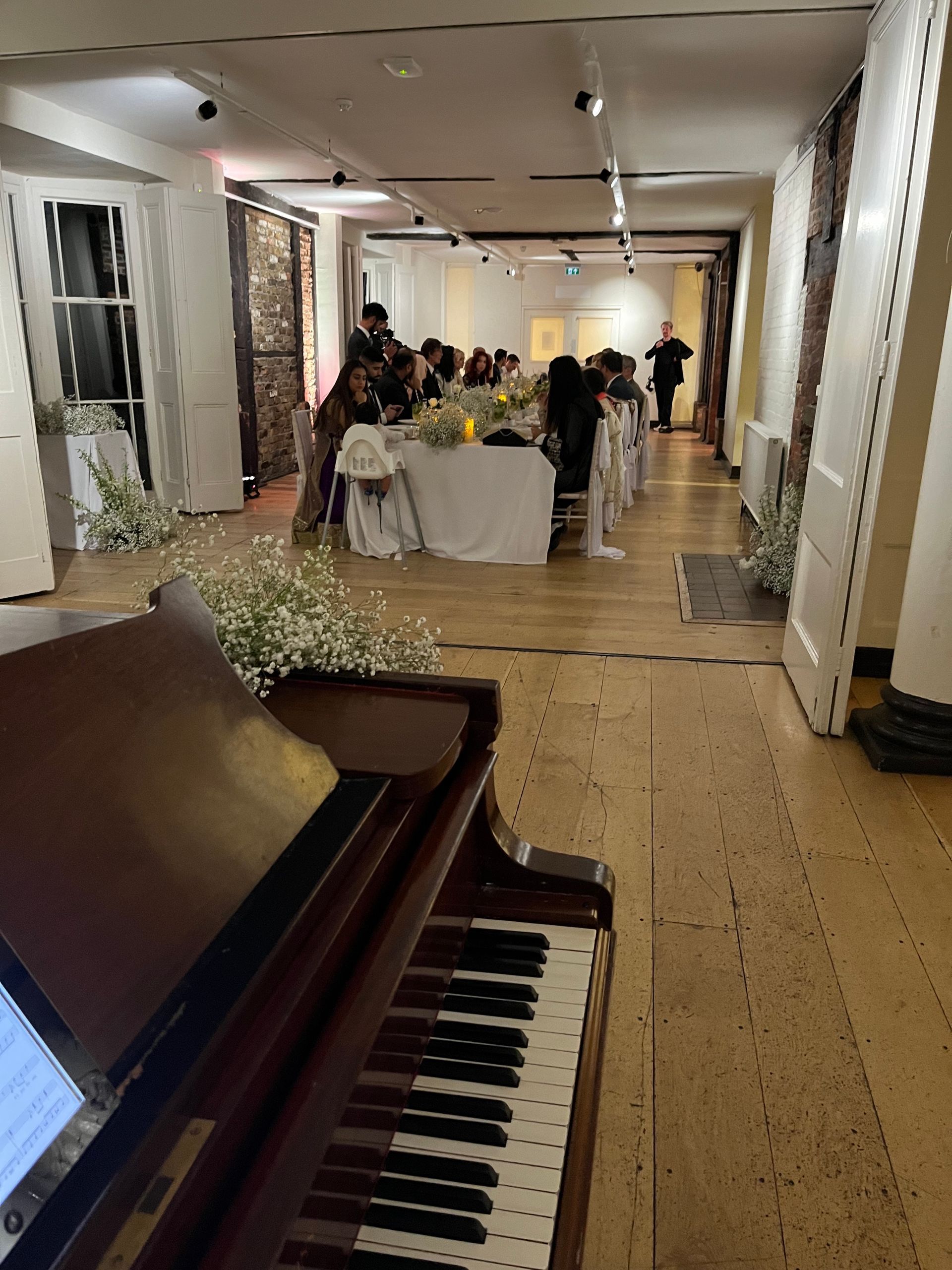 A walnut piano over looks a wedding breakfast in a hall