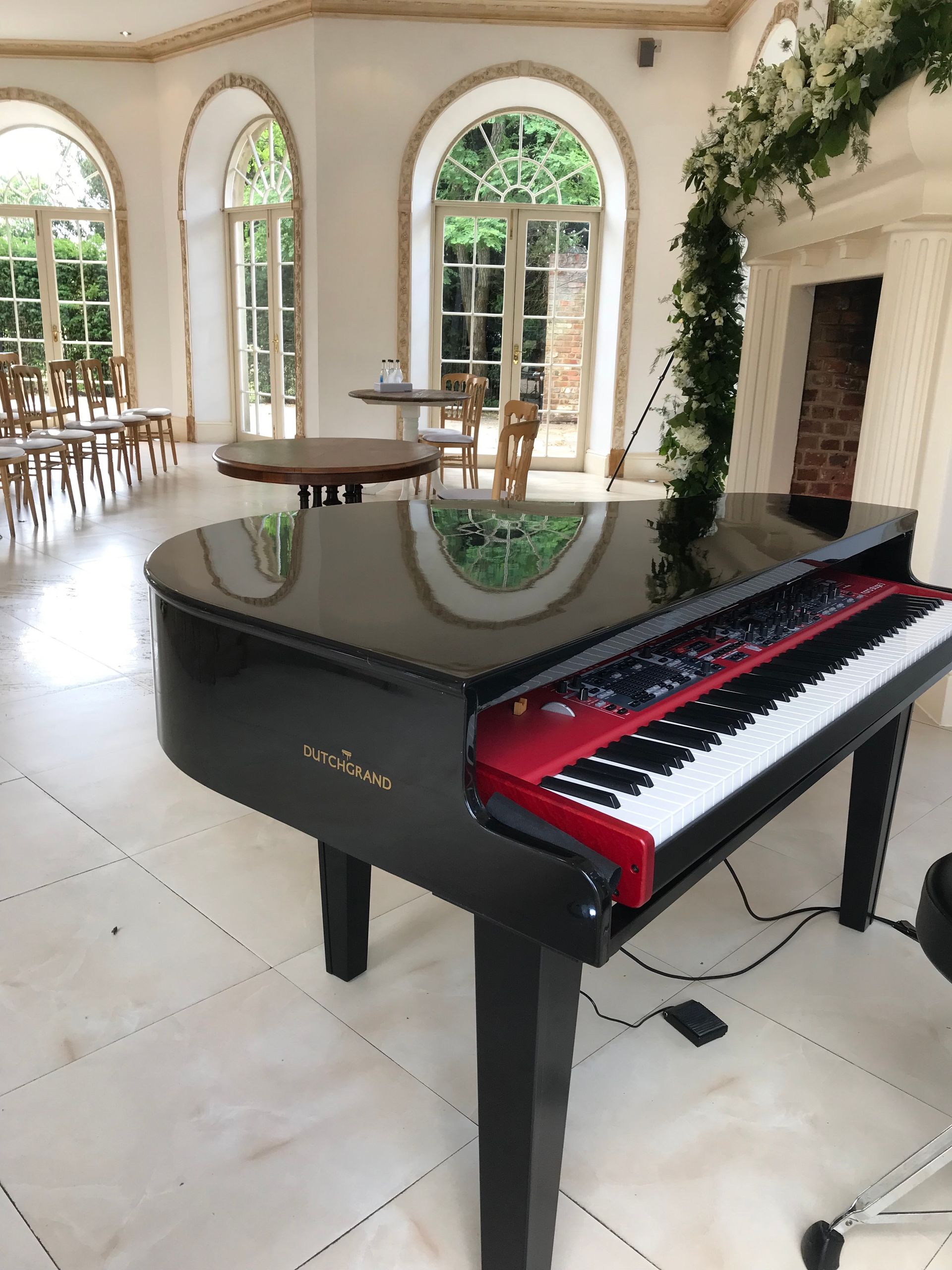 A red Nord keyboard hidden in a black baby grand piano shell in front of a fire place on a white marble floor