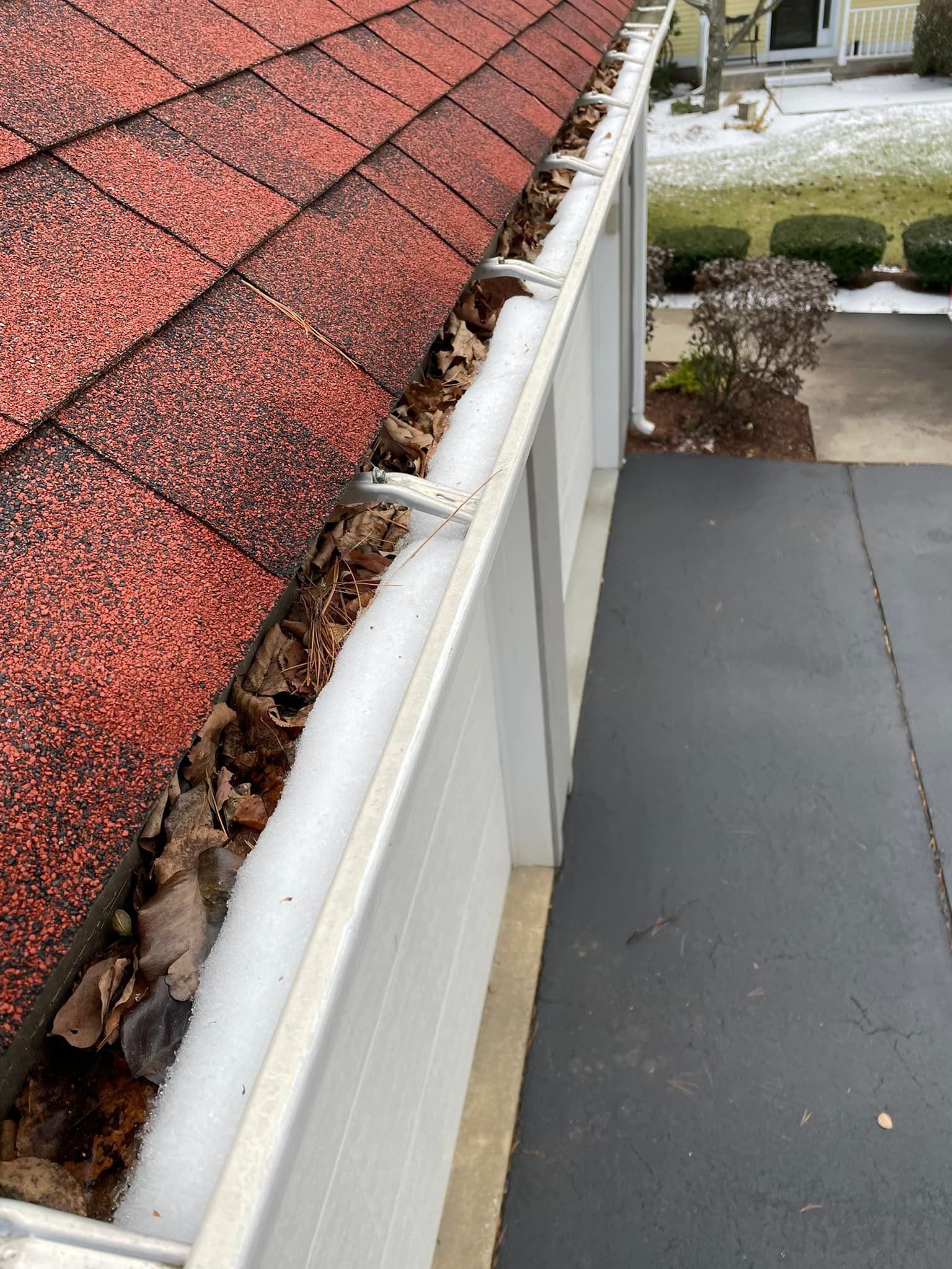 A gutter with leaves on it and a roof in the background.