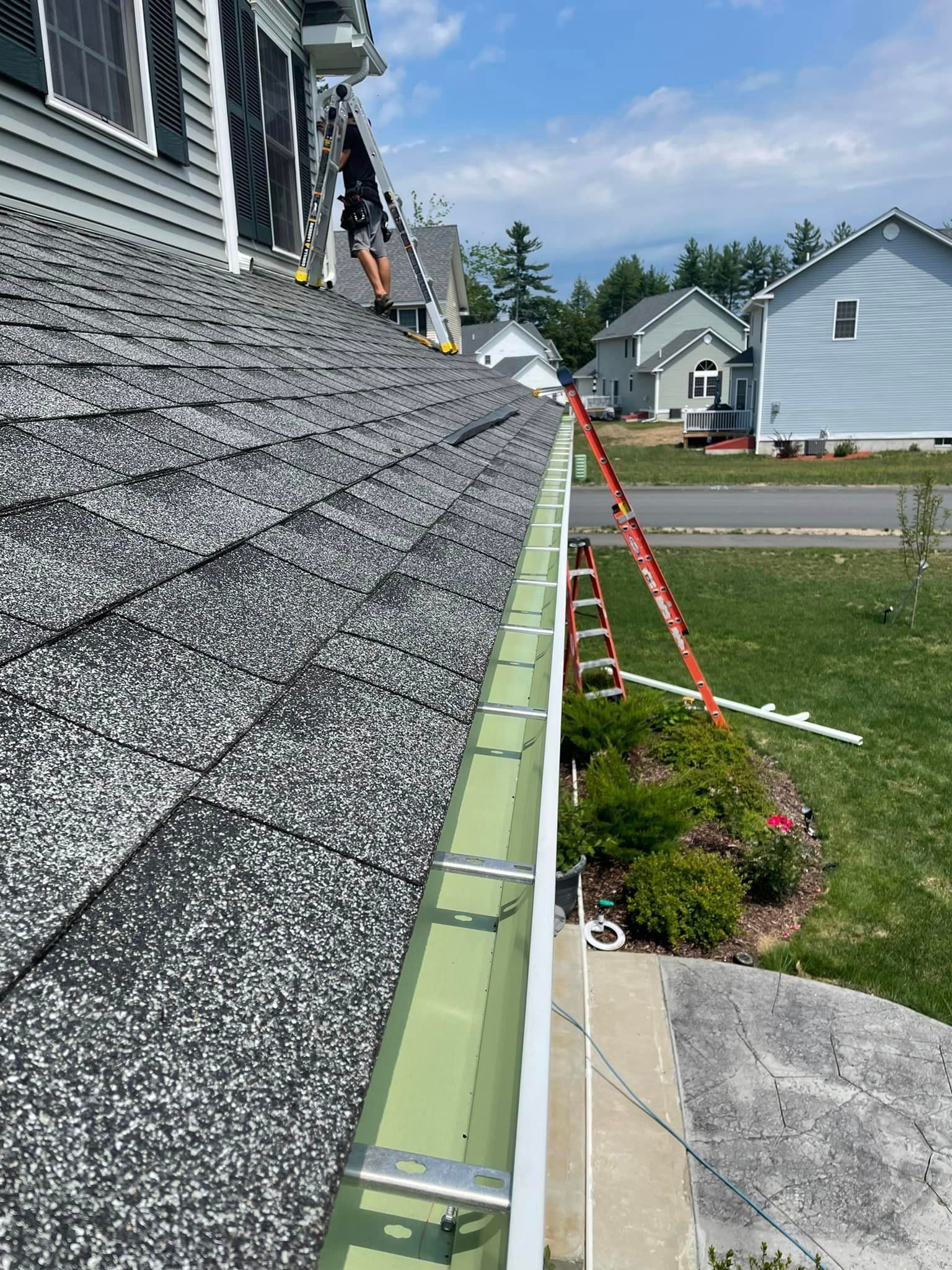 A man is standing on a ladder on the roof of a house.