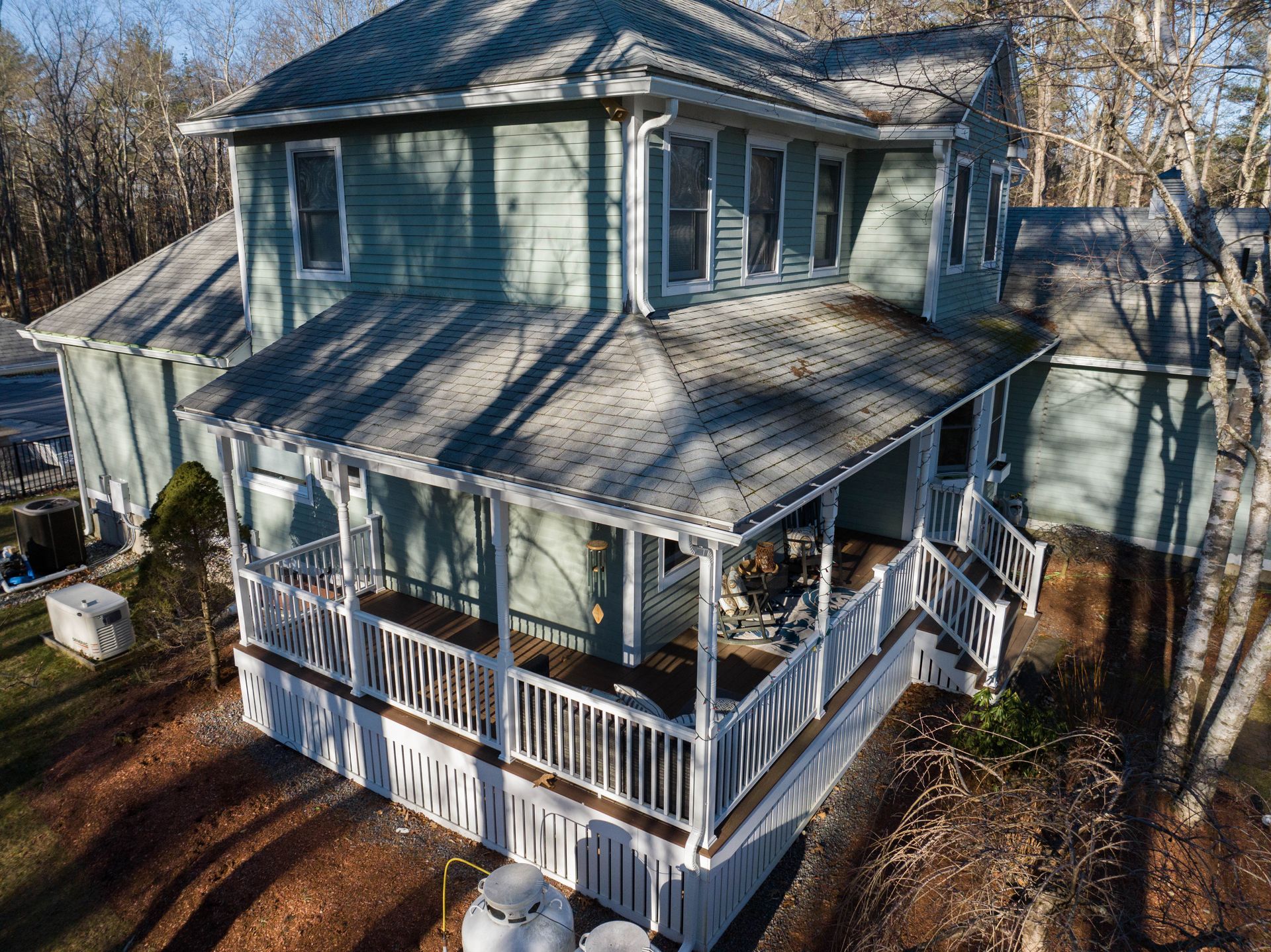An aerial view of a house with a large porch surrounded by trees.