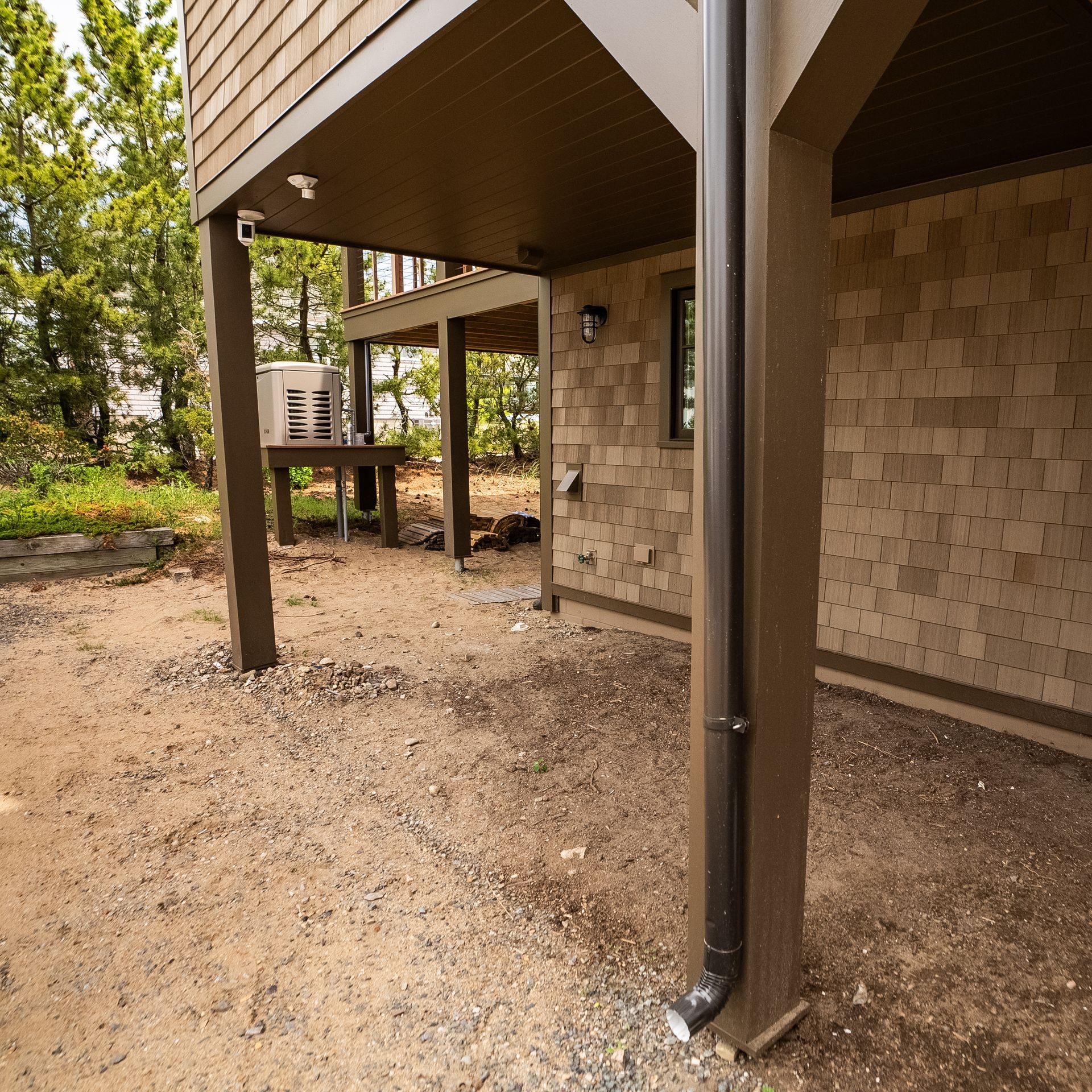 Underside of a raised house with brown support posts and gravel ground beneath the deck