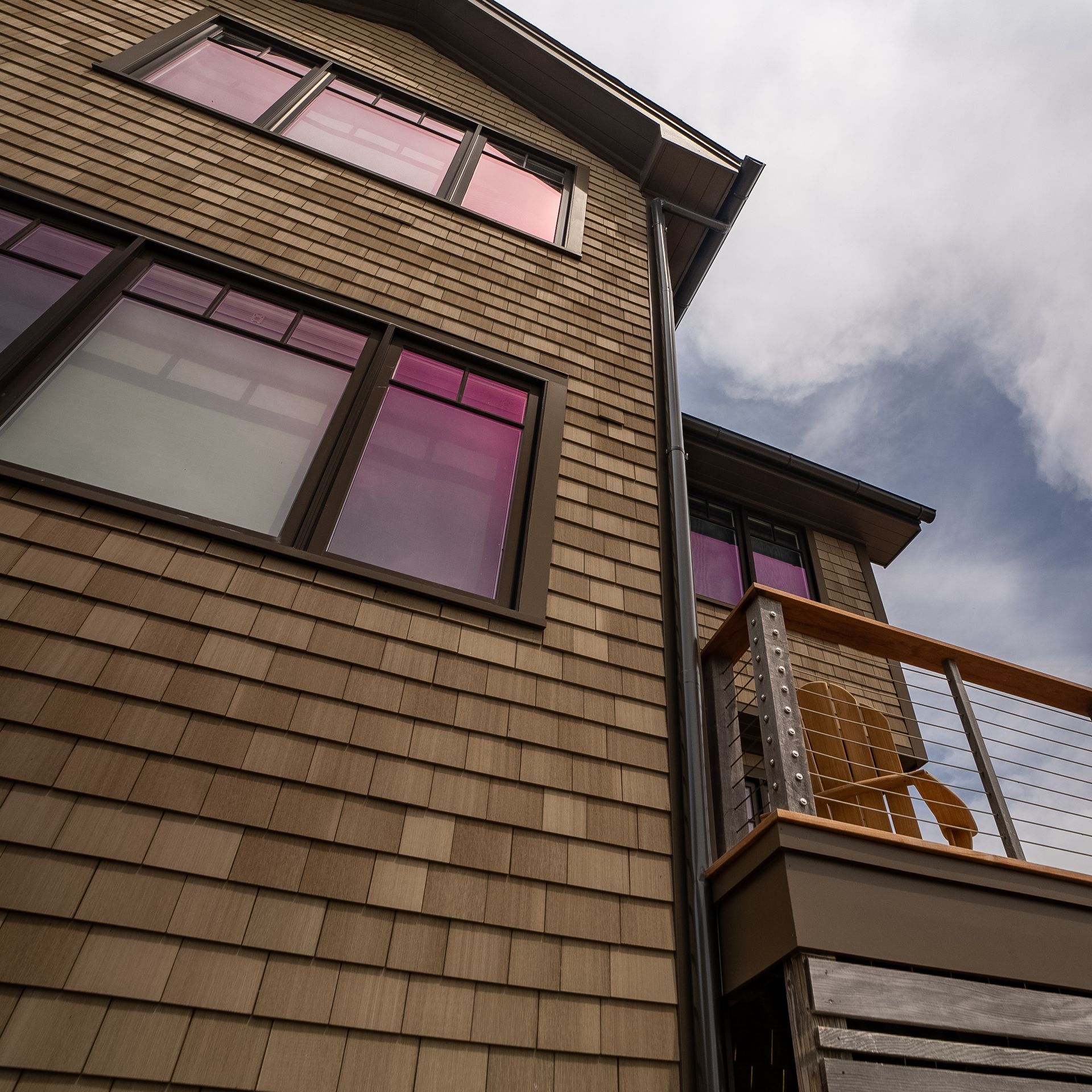 Low-angle view of a brick house with pink-tinted windows and a balcony under a cloudy sky
