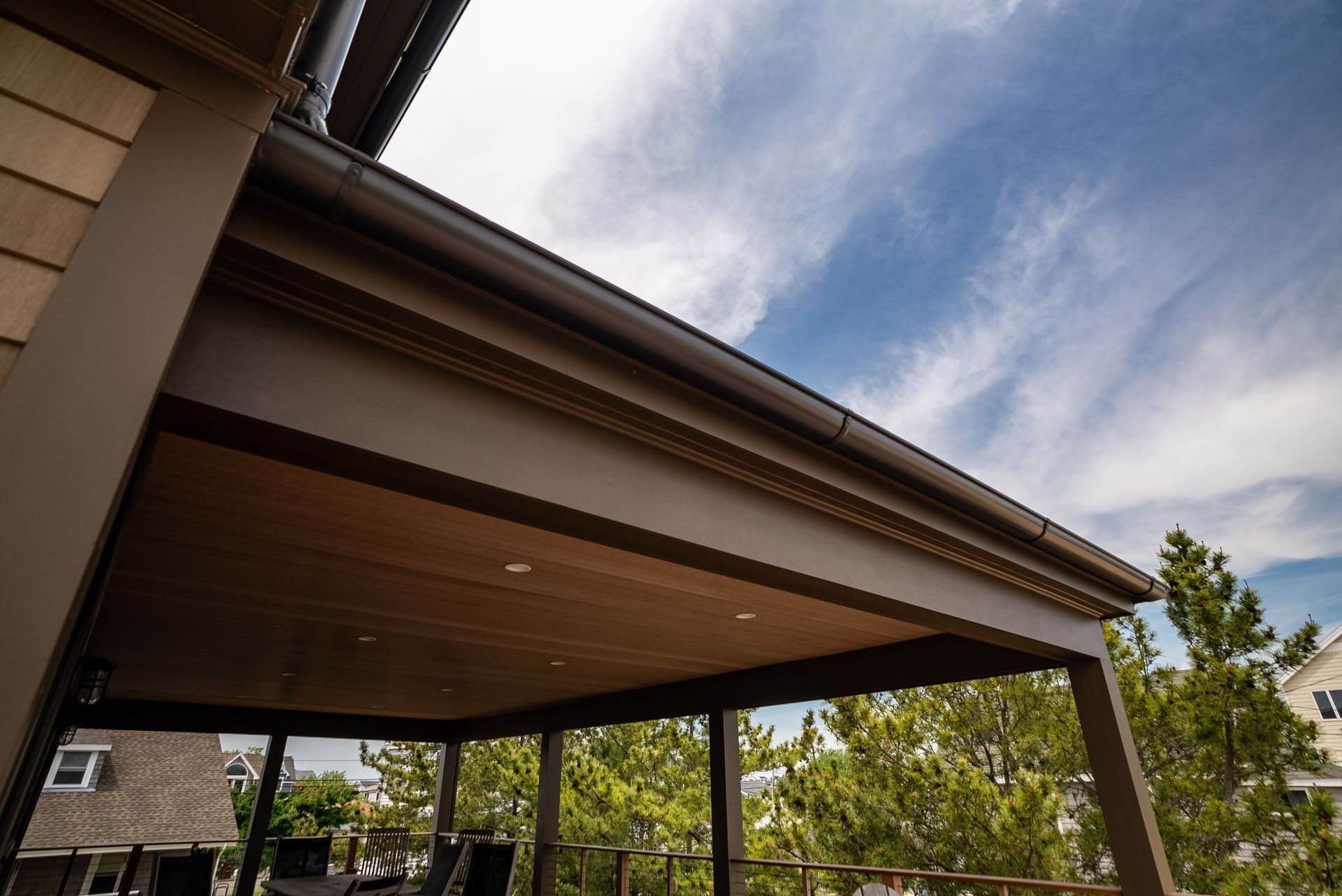 Modern house exterior with a covered patio, wooden ceiling, and blue sky above trees