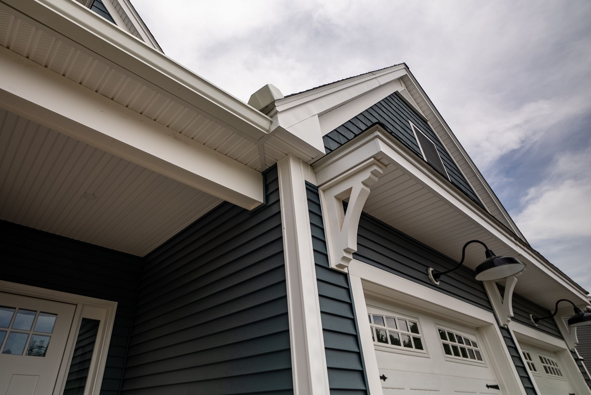 Exterior view of a dark blue house with white trim, garage doors, and gabled roofline