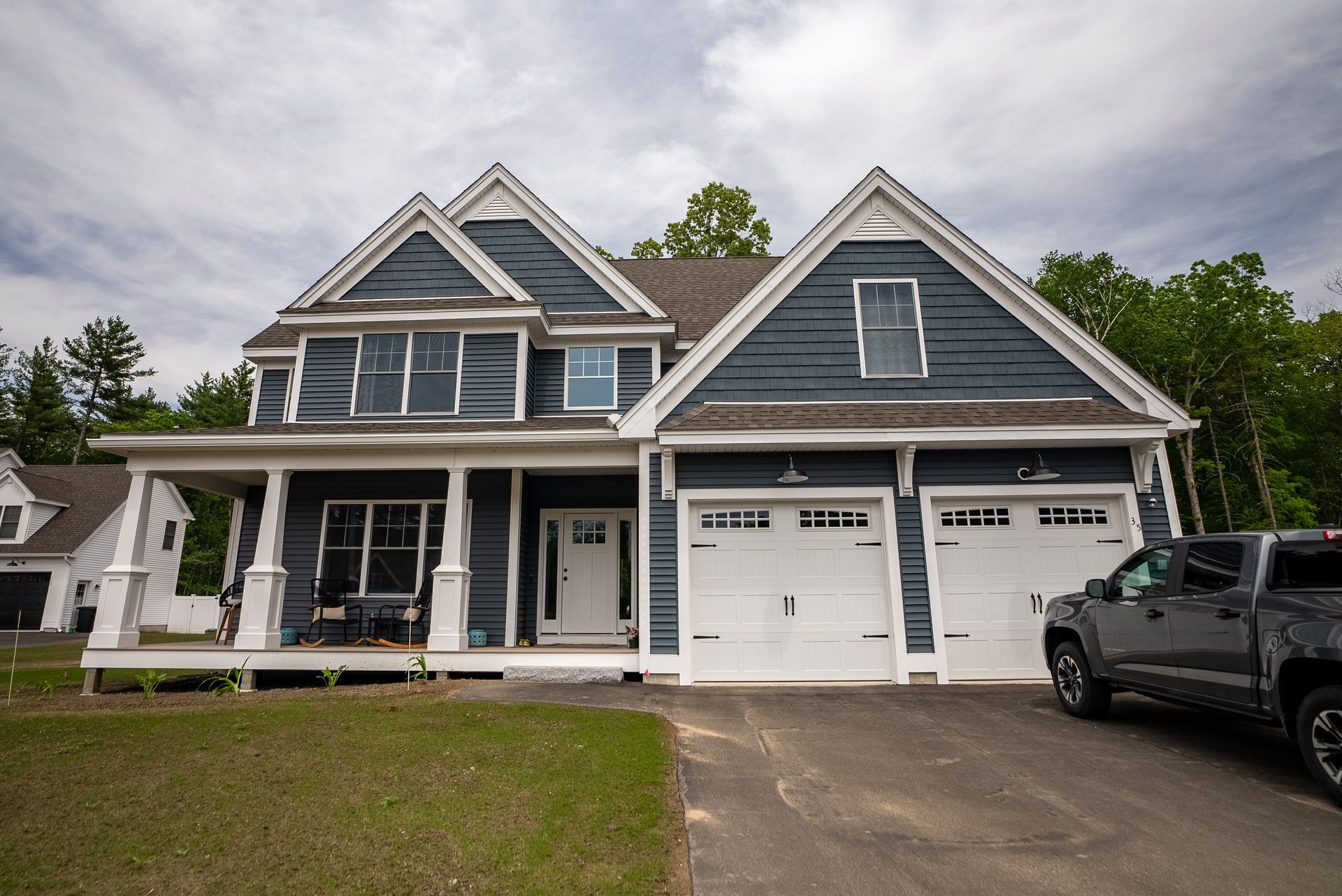 Blue-gray house with white trim, front porch, double garage, and a black pickup in the driveway