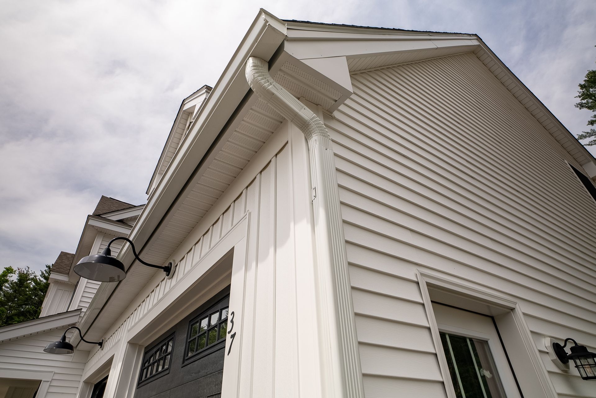 Close-up of a white house exterior with siding, gable roof, and dark window trim from a low angle