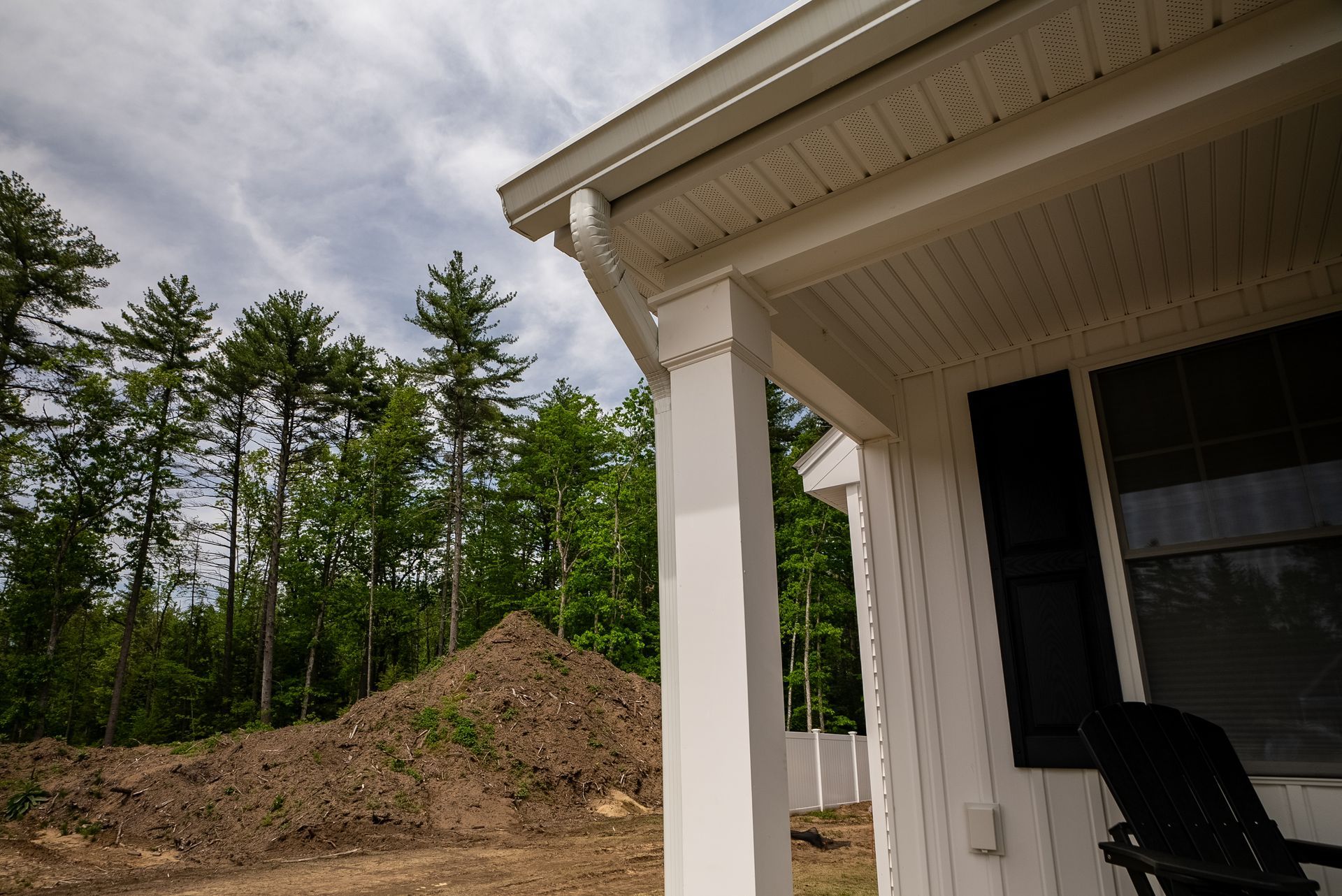 Porch corner beside a dirt mound and trees under a cloudy sky