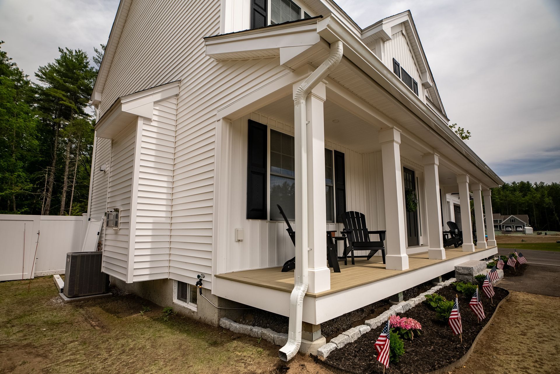 White house with a covered porch, rocking chairs, and flower beds along the front.