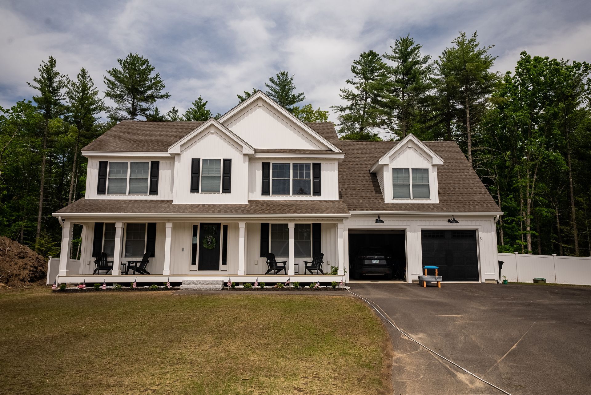 Two-story white house with a covered porch, two garage bays, and a driveway beside a wooded yard
