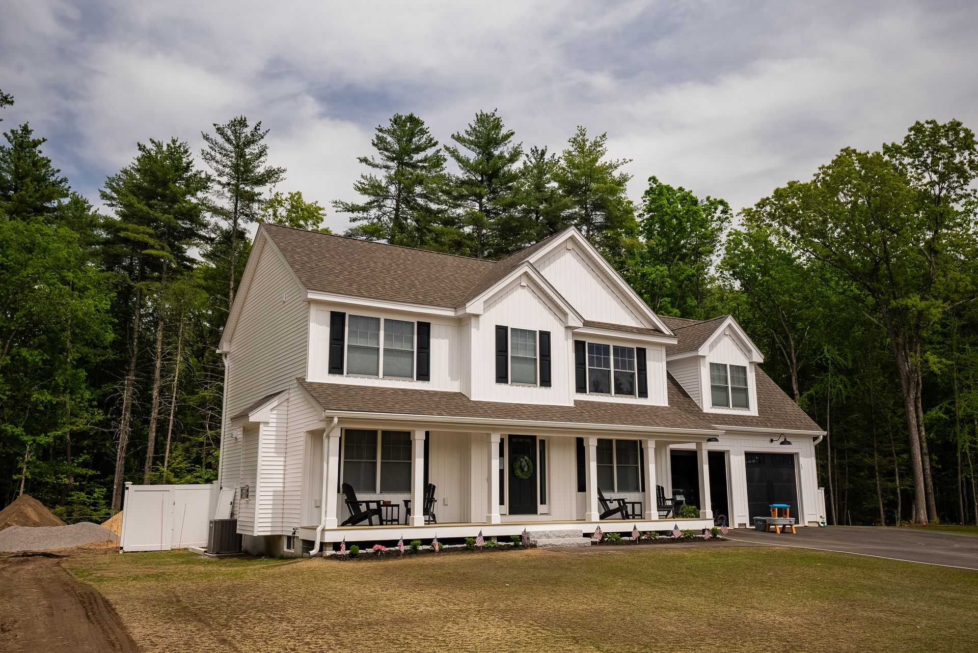 Two-story white house with black shutters and a front porch, surrounded by trees and a grassy yard.