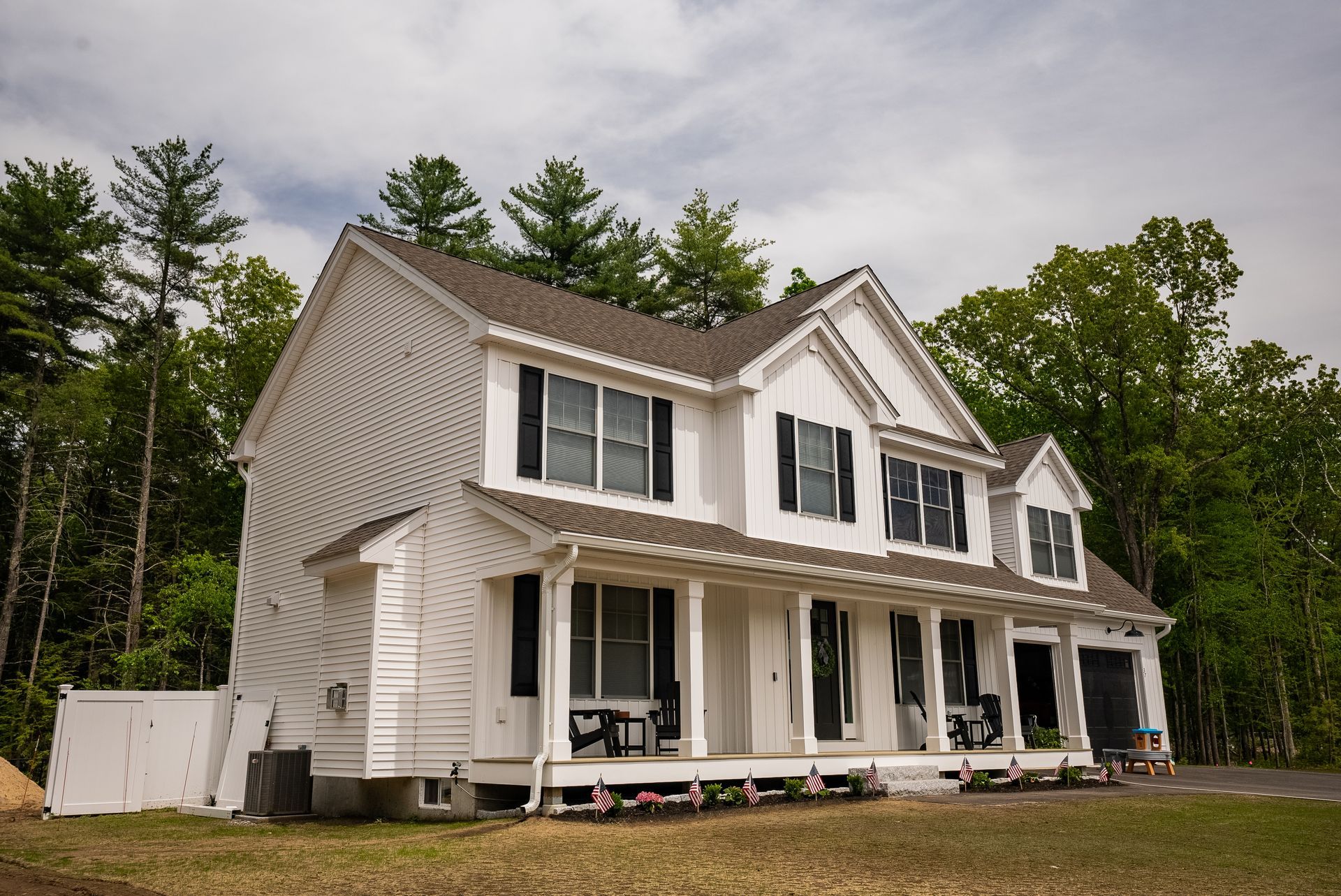 Two-story white house with a covered porch and dormer windows in a wooded yard