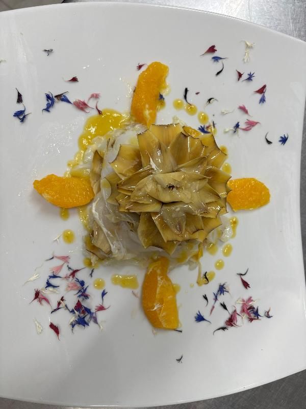 Piatto di carciofi con fette d'arancia e petali di fiori su un piatto bianco.