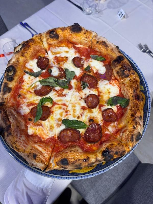 Pizza con peperoni, mozzarella, salsa di pomodoro e basilico su un piatto con bordo blu.