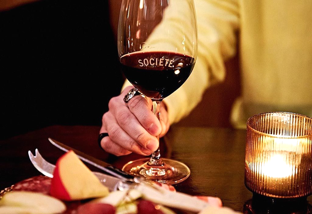 Hand holding a wine glass with red wine; charcuterie board with cheese, and candle.