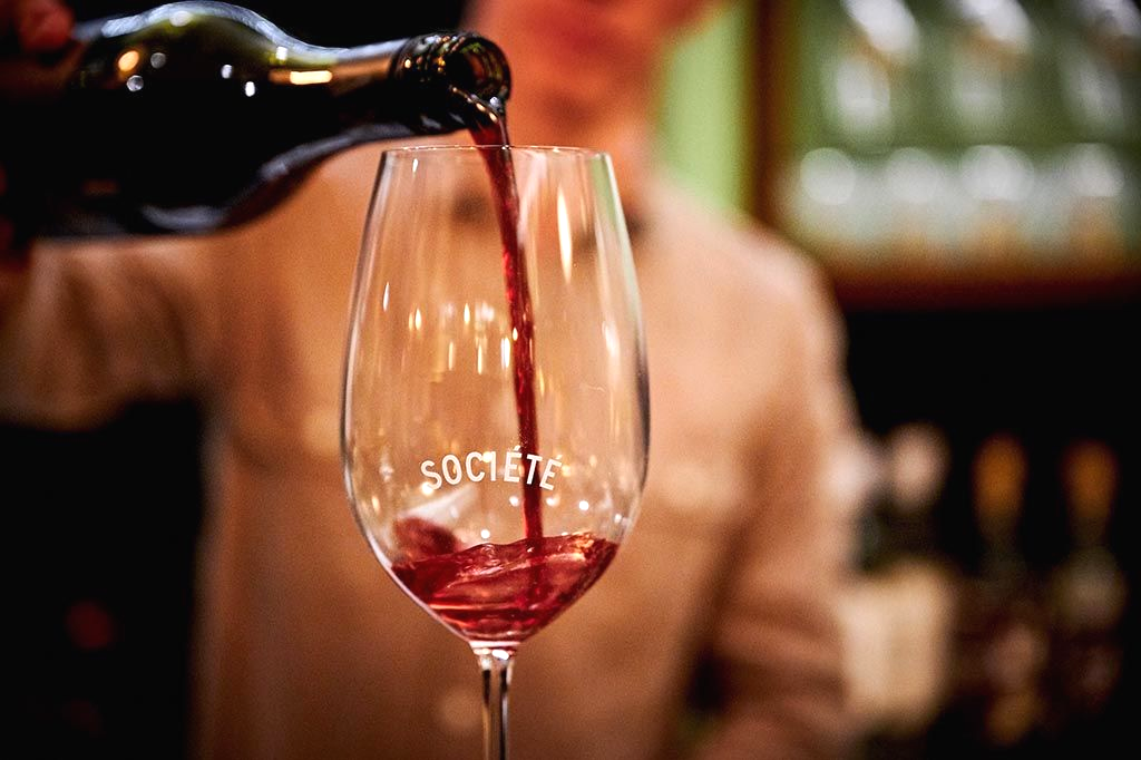 Wine being poured from a bottle into a clear glass in a dimly lit bar.