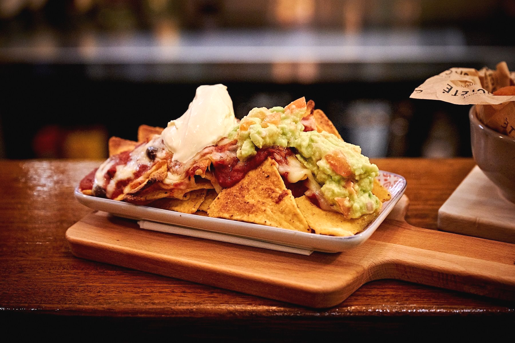 Nachos on a wooden serving board, topped with cheese, salsa, and guacamole.