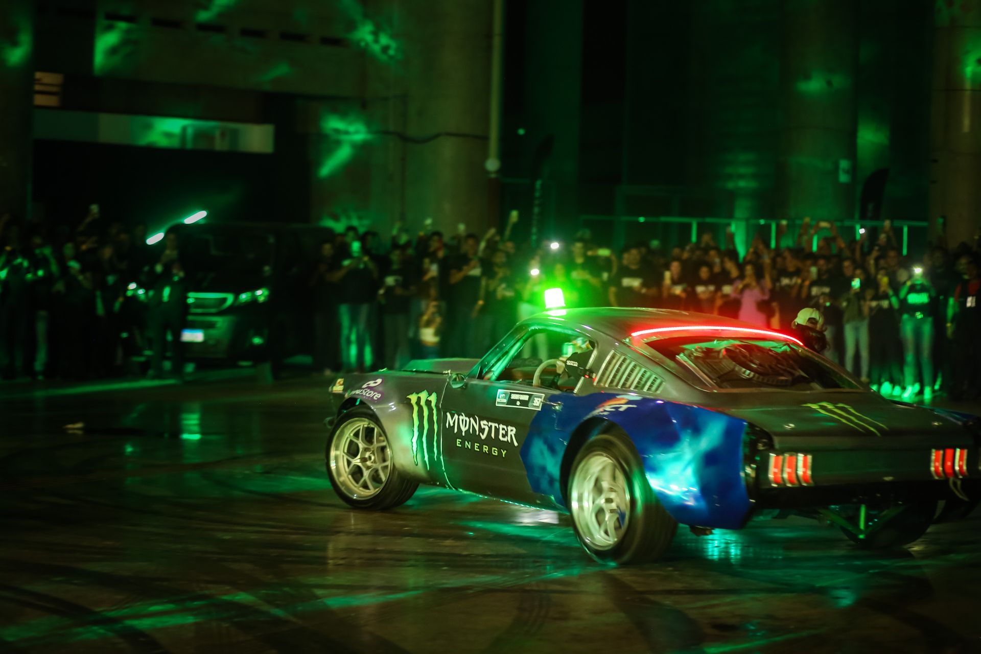 Um carro elétrico monstruoso está descendo uma rua na frente de uma multidão.