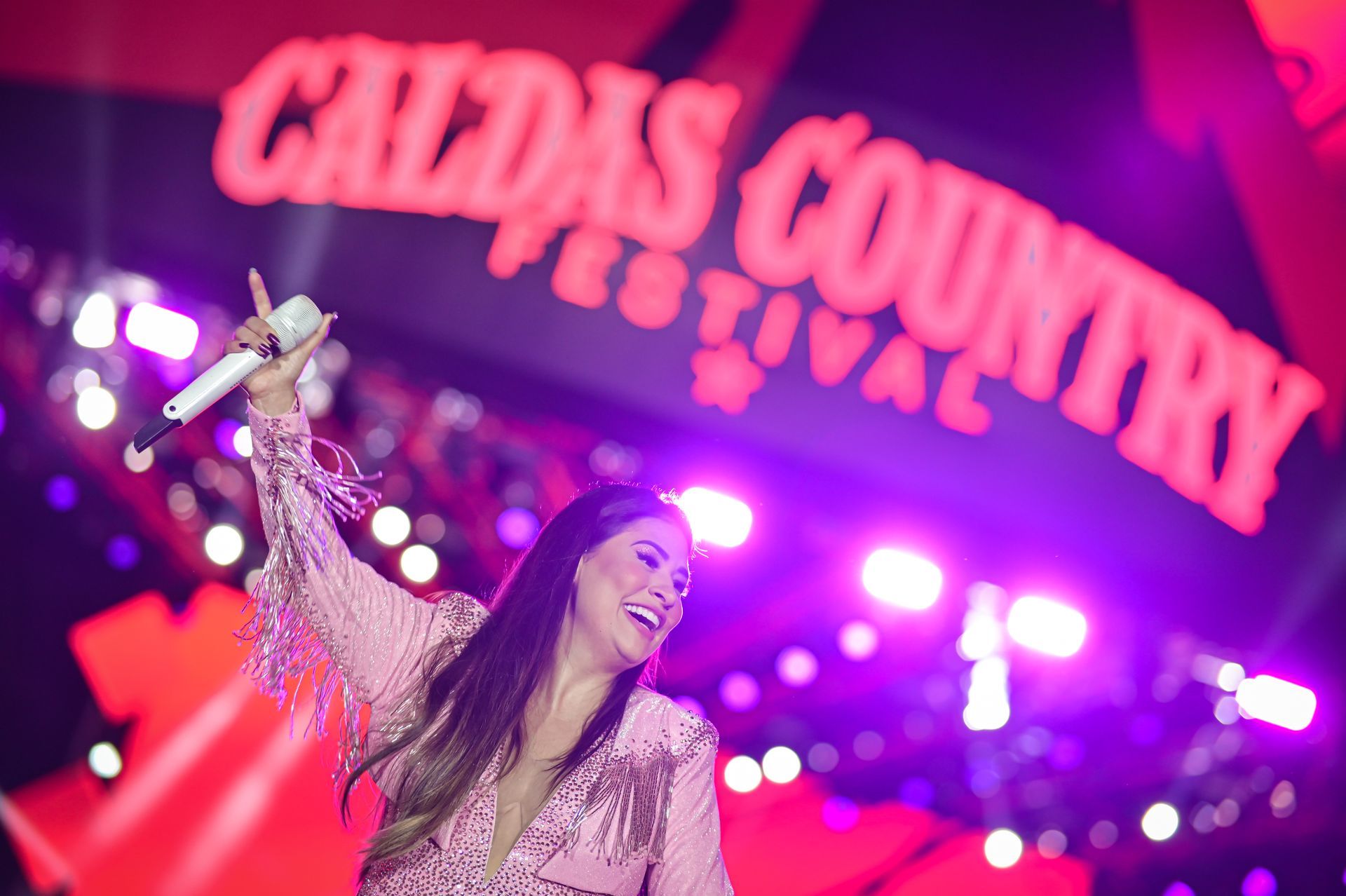 Uma mulher está cantando em um microfone em um palco em frente a uma placa que diz festival country de caldas.