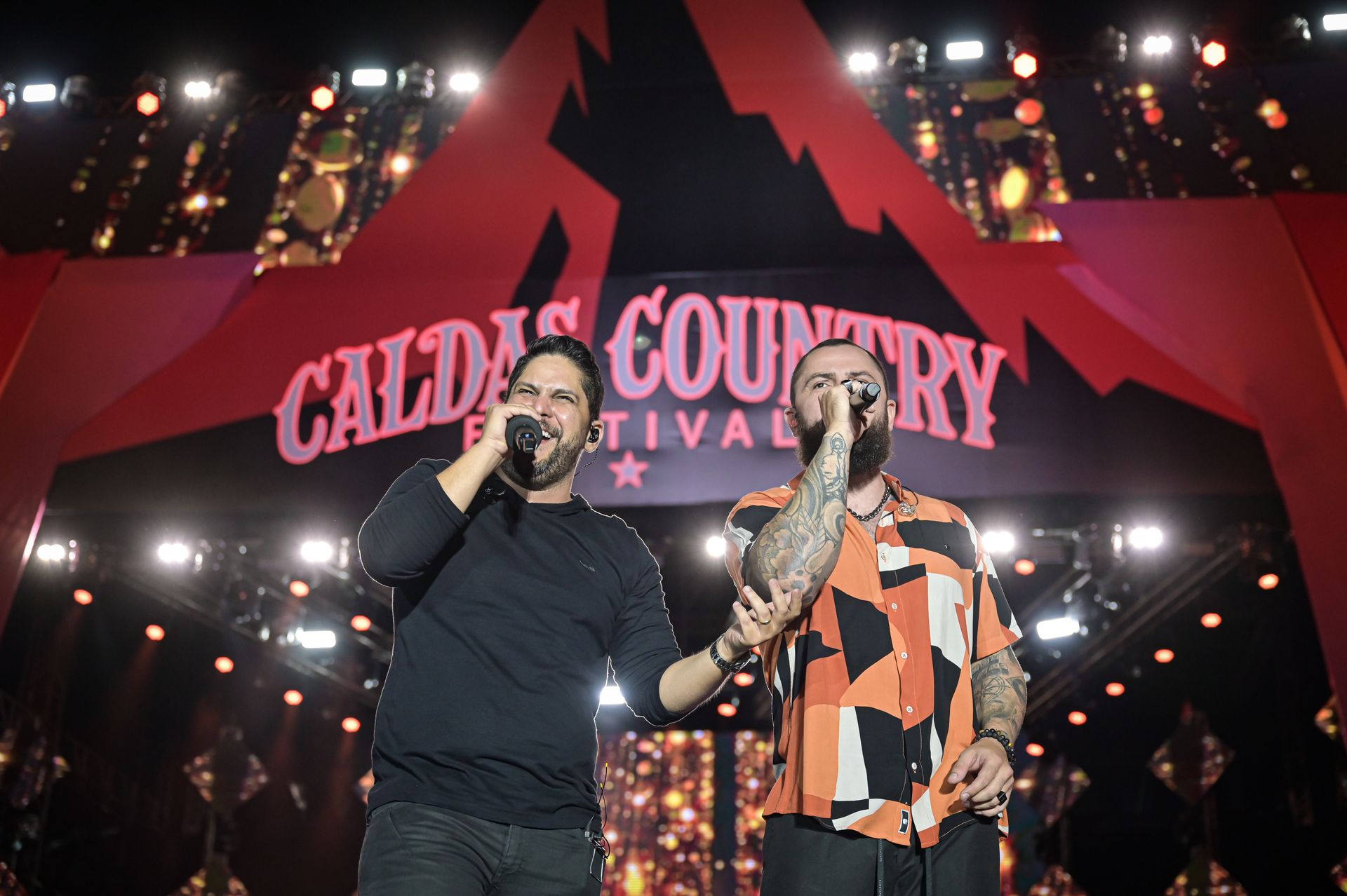 Dois homens estão cantando em microfones em um palco.