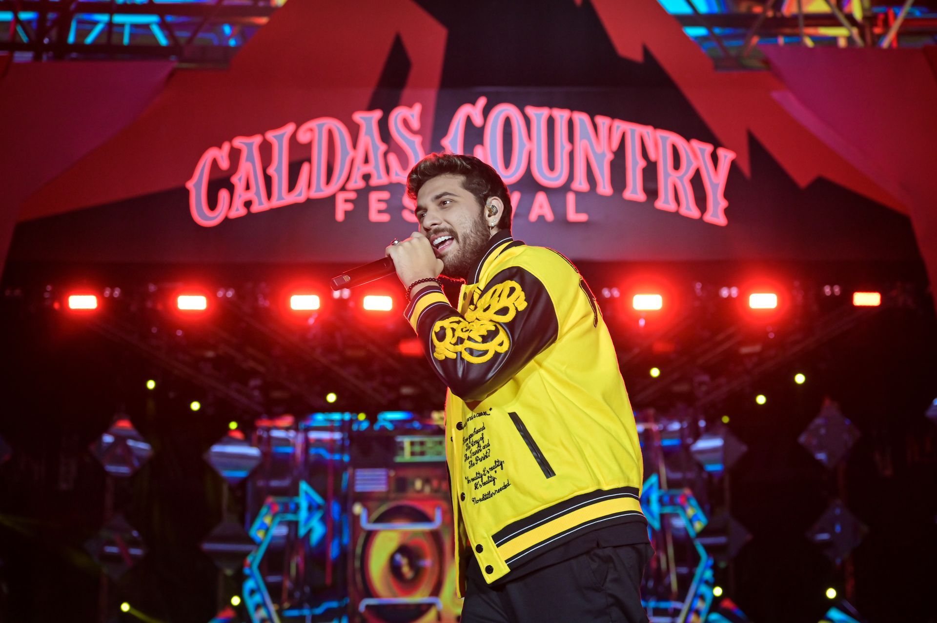 Um homem está cantando em um microfone em frente a uma placa que diz festival country de caldas