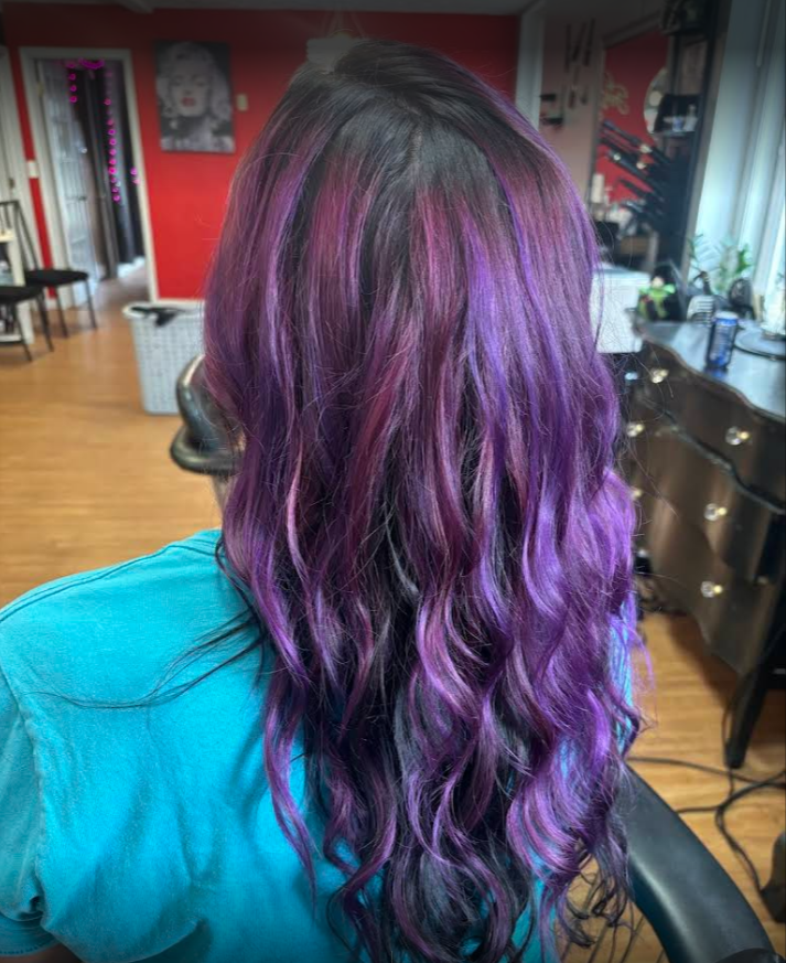 A woman with purple hair is sitting in a chair in a salon.