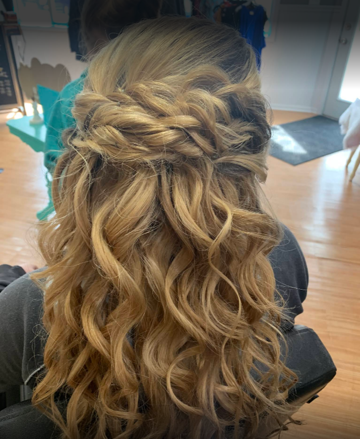 A woman is sitting in a chair with her hair in a half up half down hairstyle.